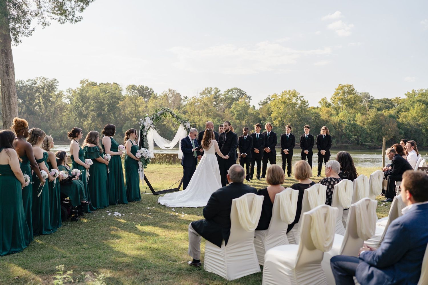 Panoramic view of outdoor wedding ceremony seating with white covered chairs against a natural landscape.