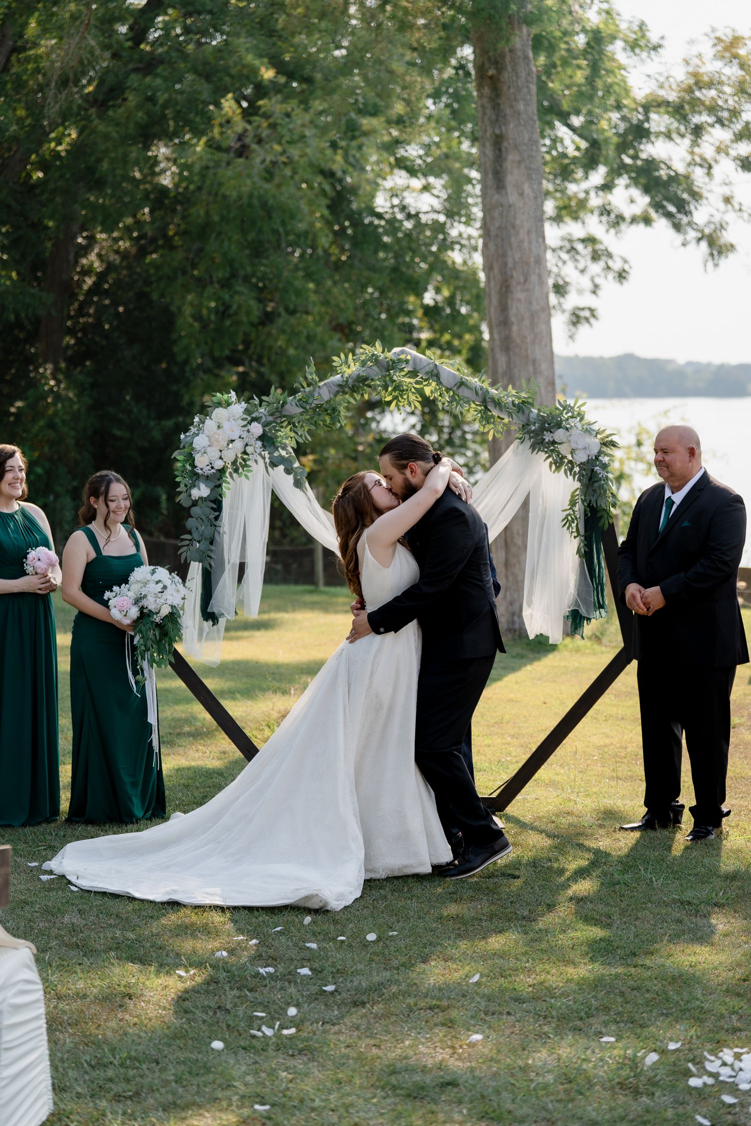 A series of wedding photos showing a couple's first kiss and celebration at an outdoor lakeside ceremony with white decor.