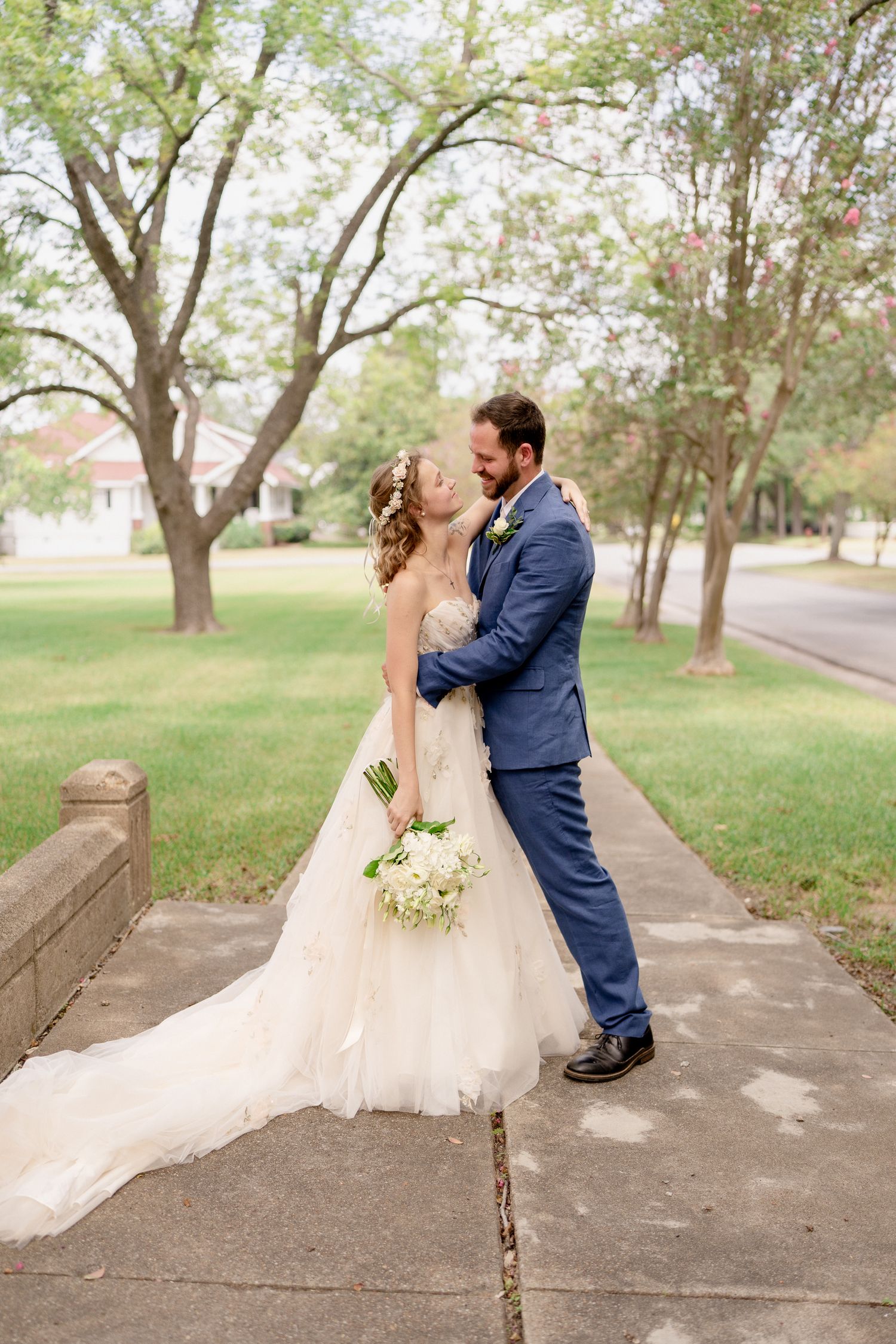 A romantic wedding couple shares an intimate kiss while sitting on stone steps in a park setting.