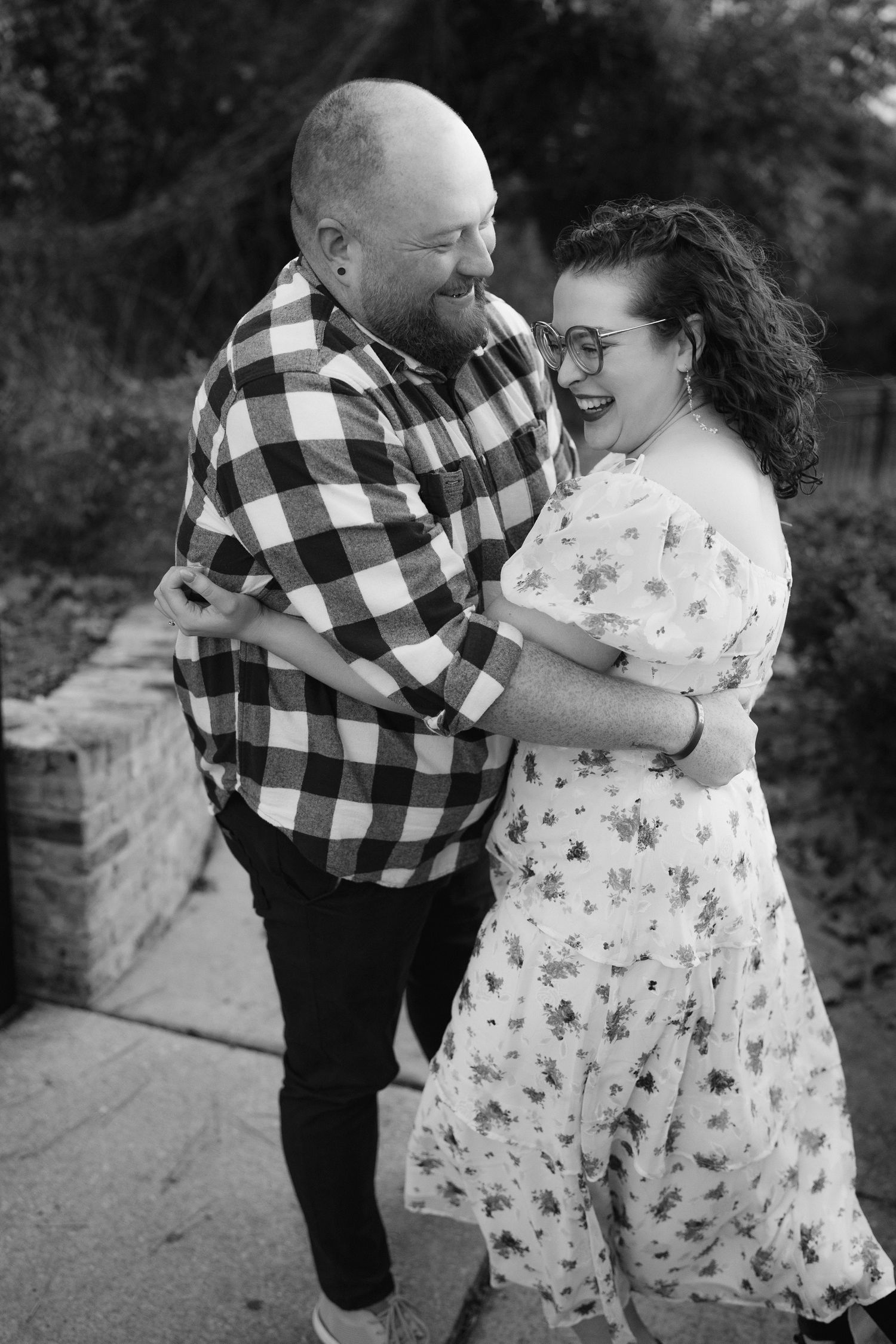 A black and white photo captures a couple sharing a joyful embrace outdoors.