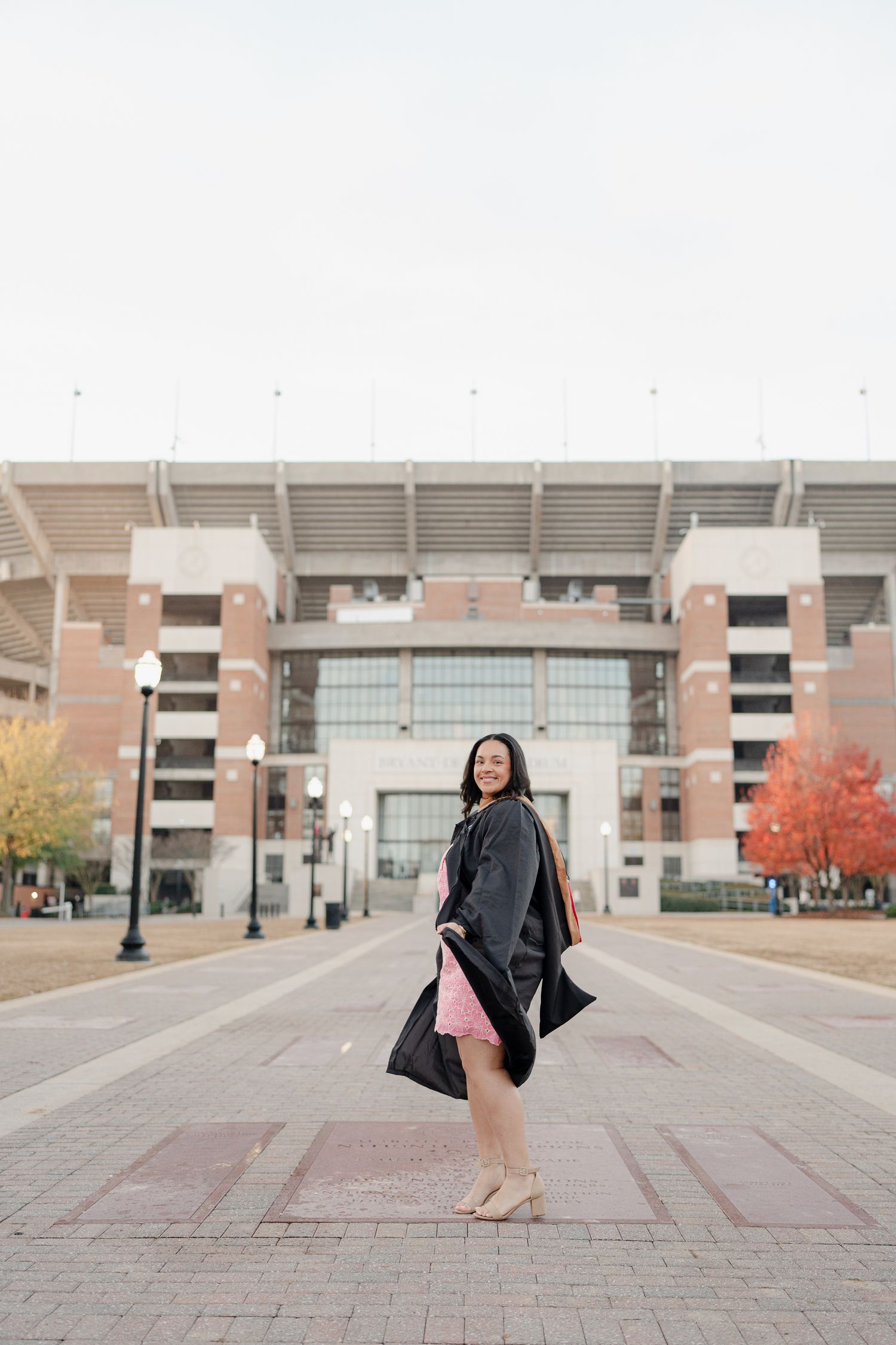 A series of graduation photos taken outside a brick stadium or arena building on a sunny day.