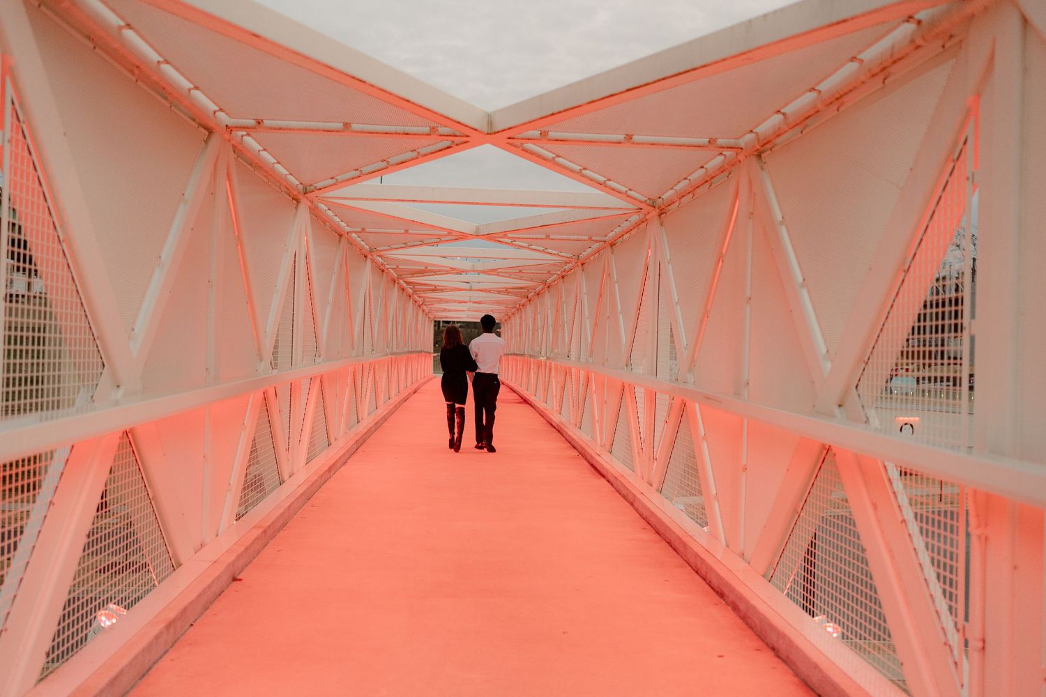 A couple walks through a vibrant red-lit pedestrian bridge tunnel together.
