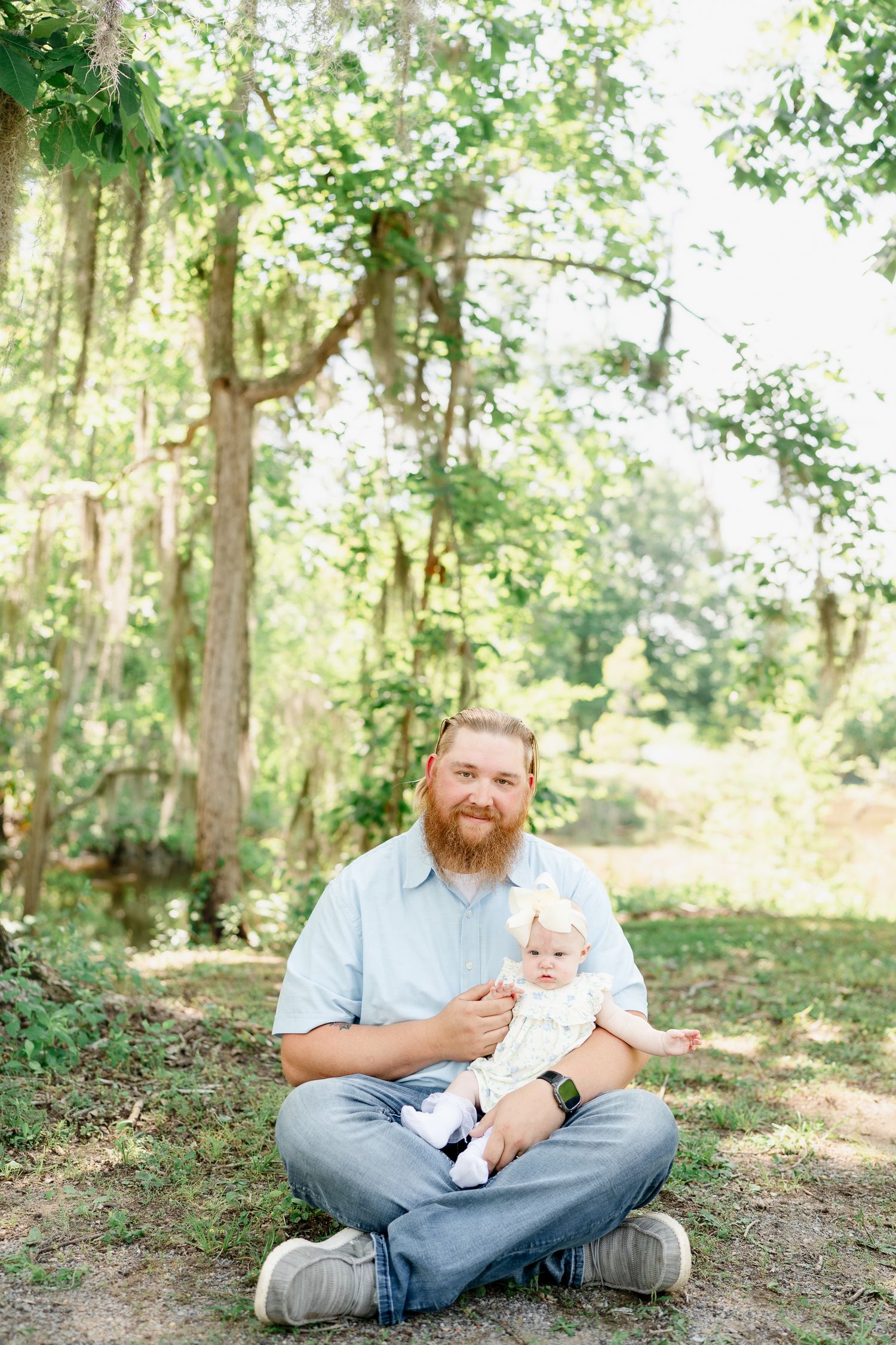 Parent and baby sharing tender moments during outdoor photoshoot in wooded setting.