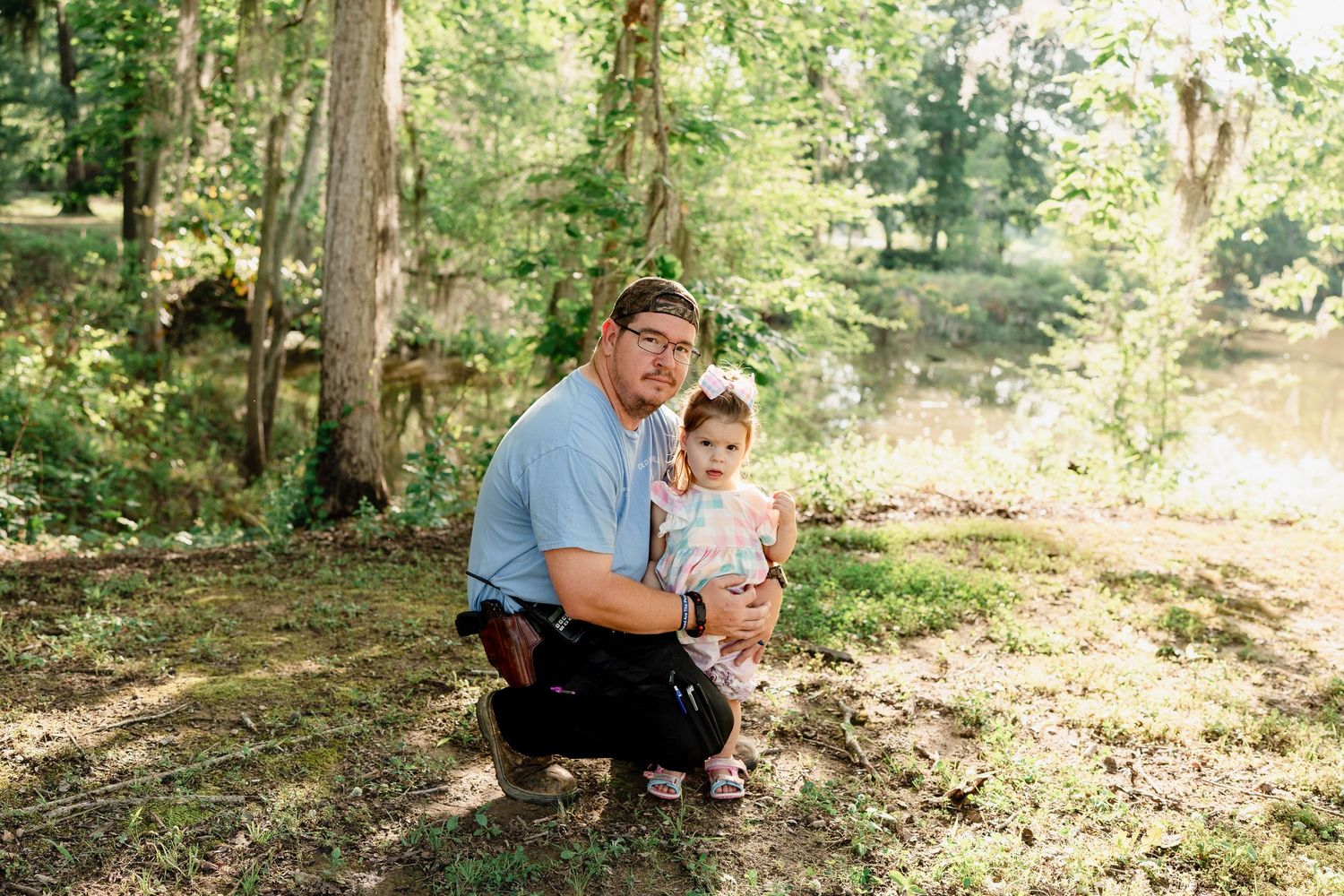 Parent and child share a tender moment while kneeling in a sunlit forest.