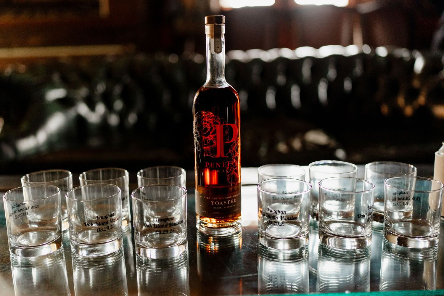 Red liquor bottle surrounded by empty cocktail glasses on reflective surface.