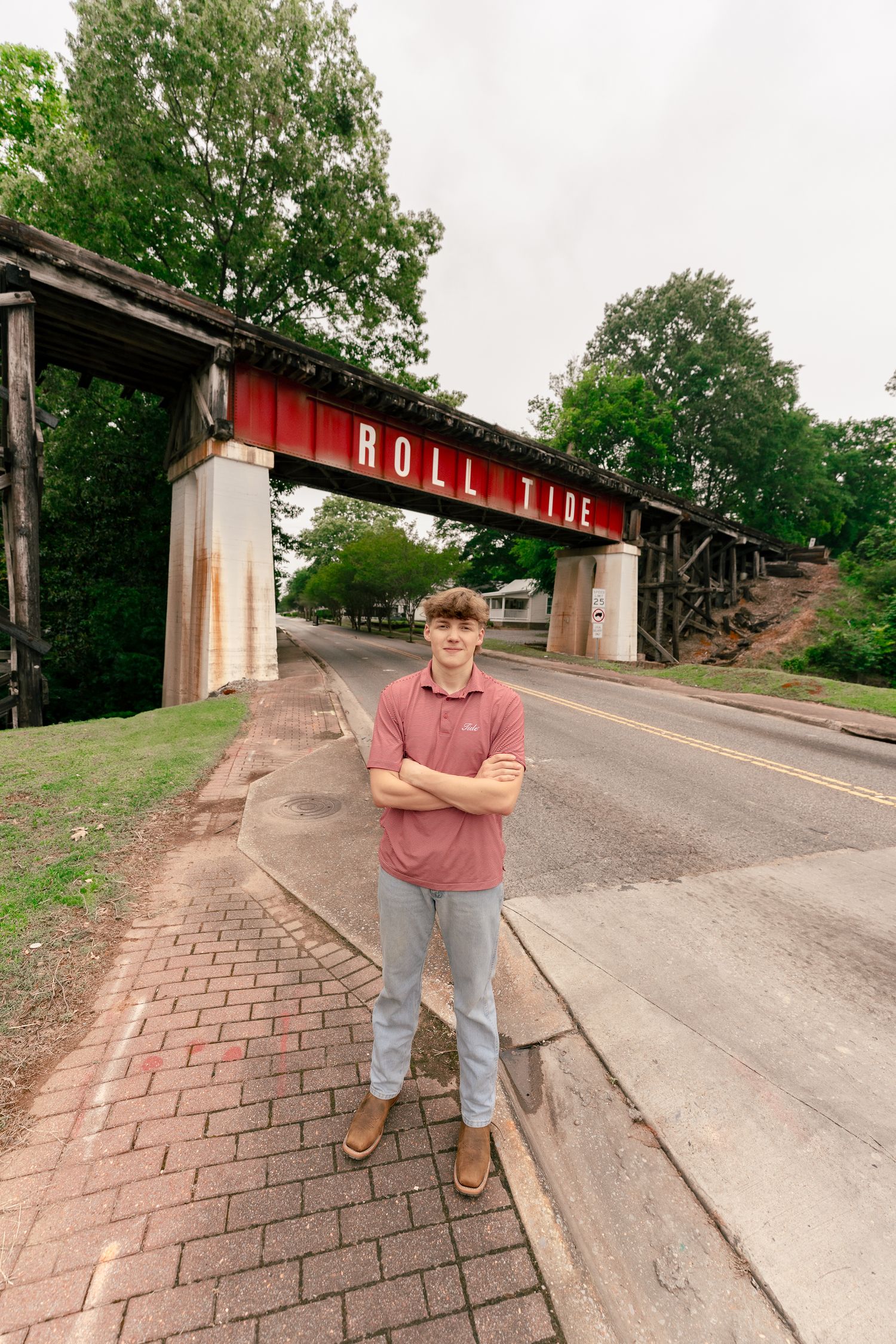 A brick walkway leads to a bridge structure displaying 'Roll Tide' text with someone standing nearby.