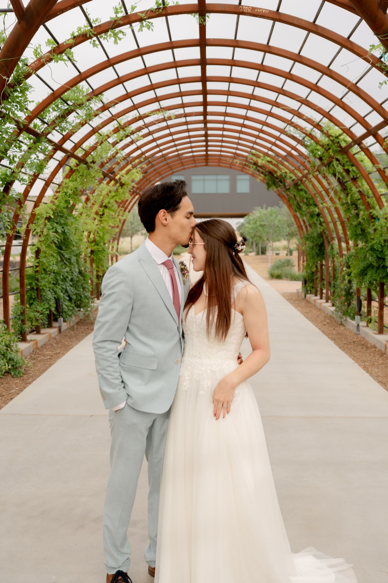 Newlyweds embrace in a romantic moment beneath an arched garden tunnel walkway.