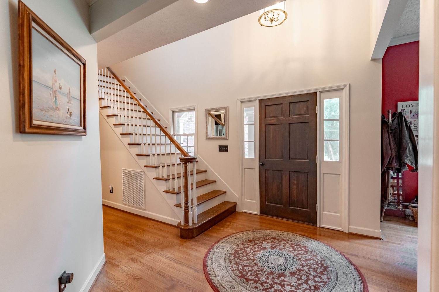 Elegant foyer entrance with hardwood floors, white walls, curved wooden staircase and a decorative round area rug.
