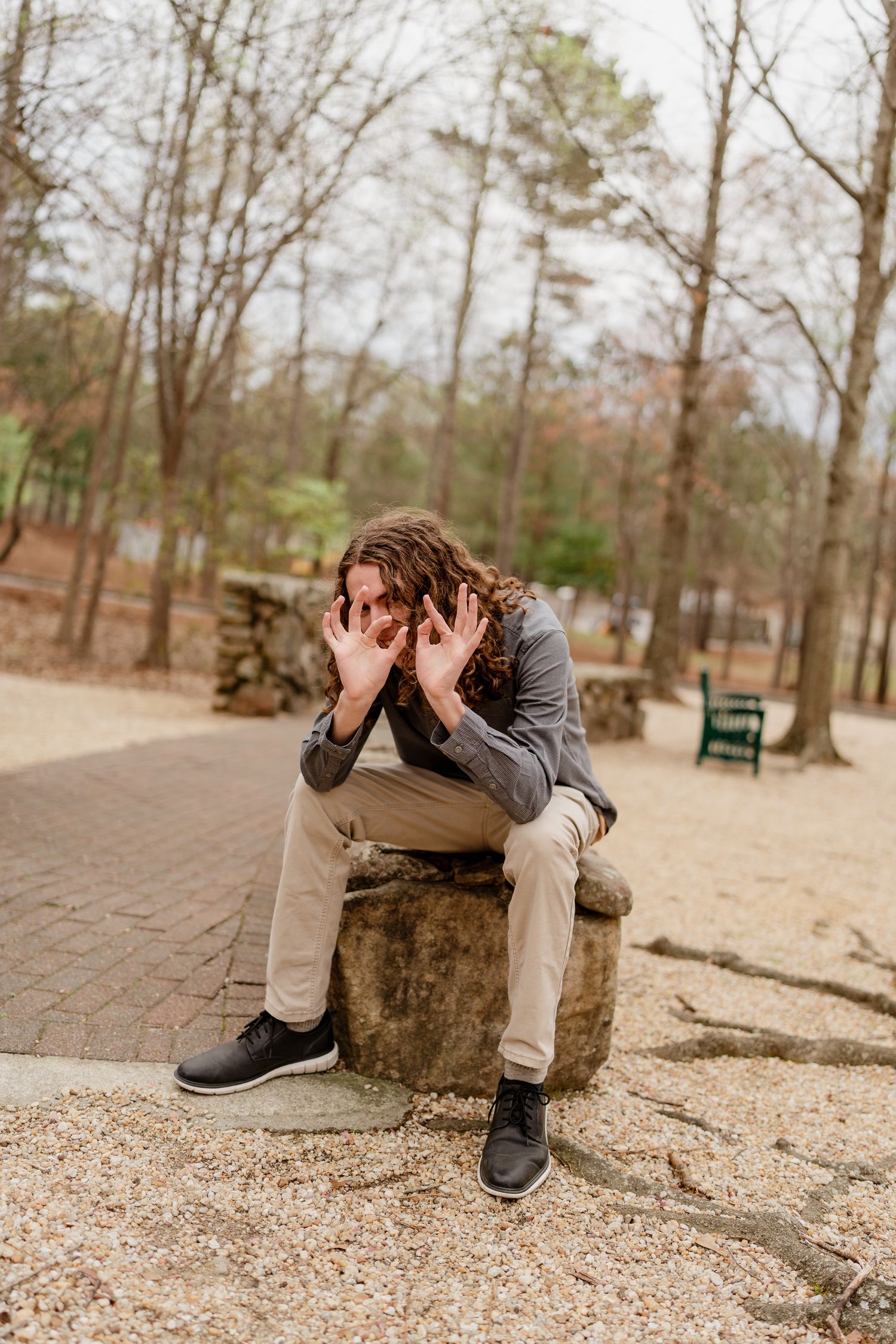 Person sitting on a tree stump with hands covering face in an artistic pose.