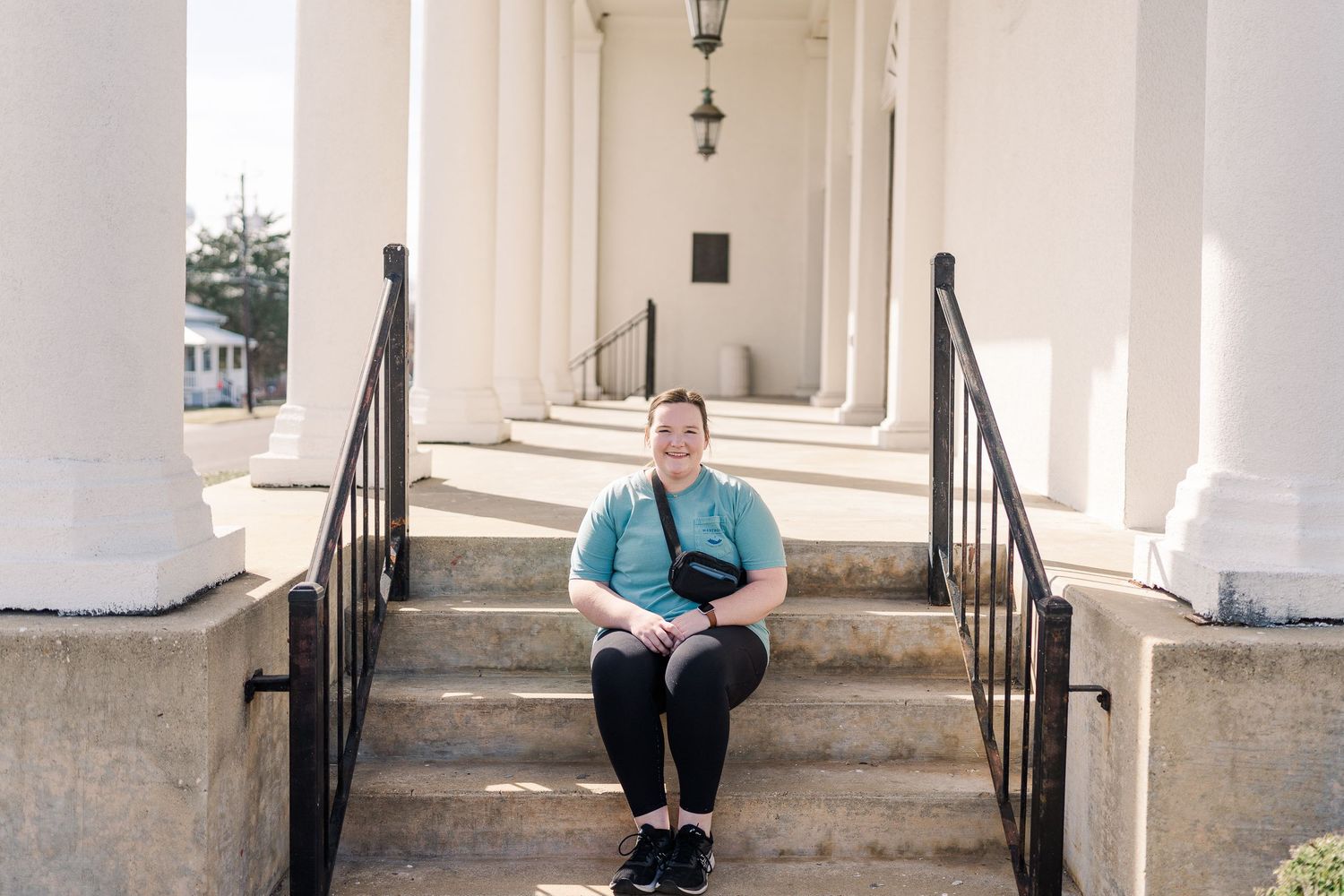 Person sitting on white church steps with columns and railings.