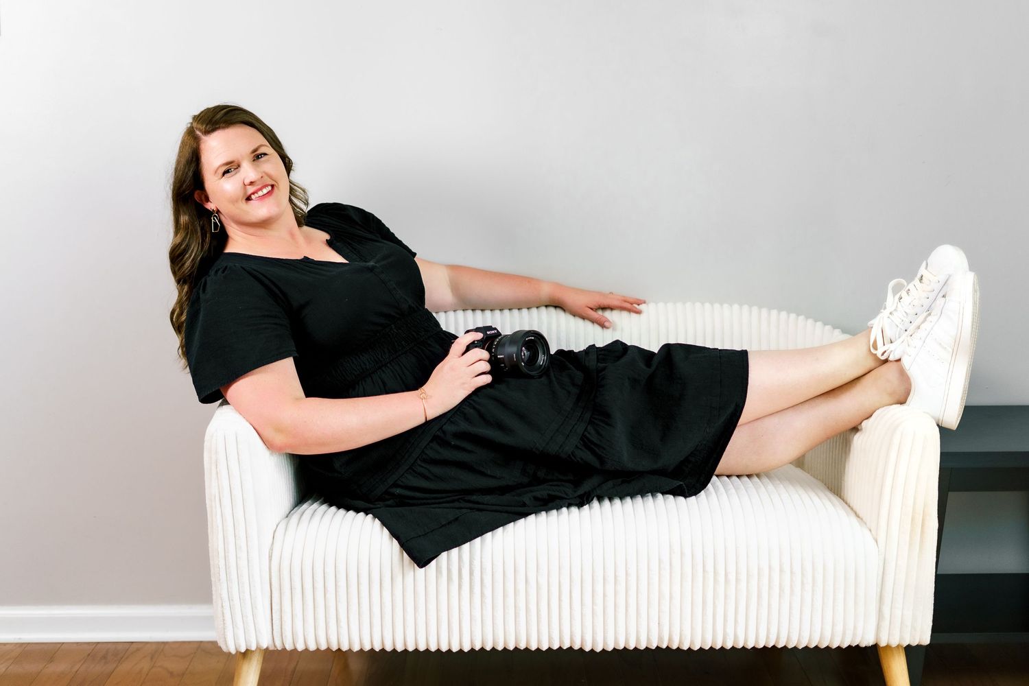 A person in black reclines on a white modern couch during a lifestyle photography session.