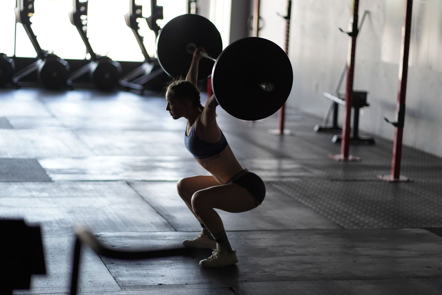 Athletic figure performing a front squat with barbell in moody gym lighting.