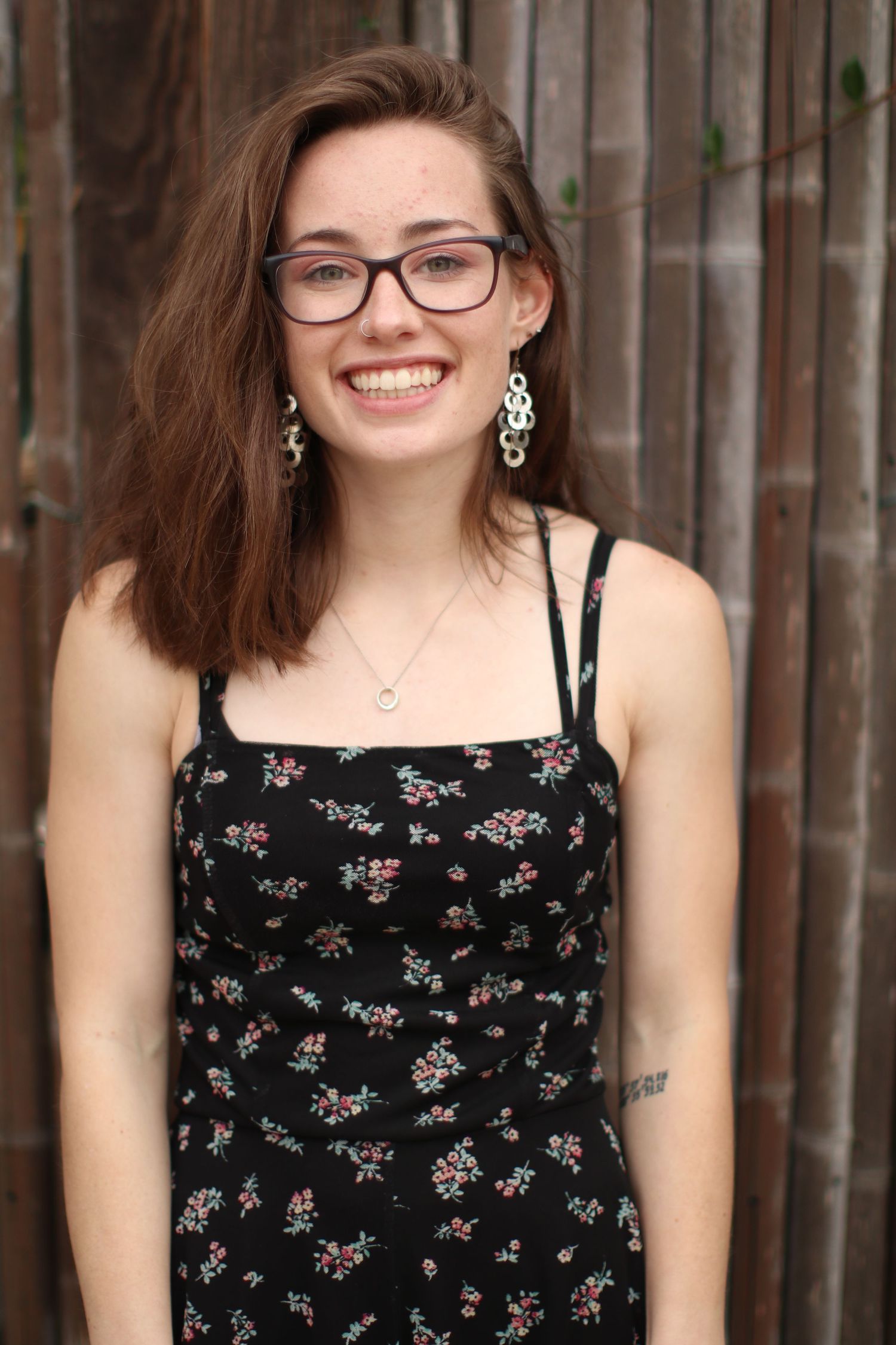 Stylish portrait of someone wearing glasses and a floral patterned dress with dangling earrings.