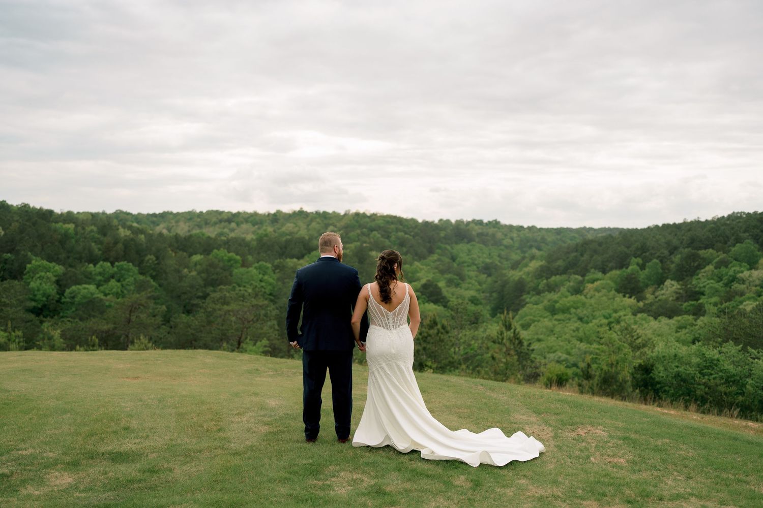 Bride and groom standing together overlooking scenic green valley on their wedding day.