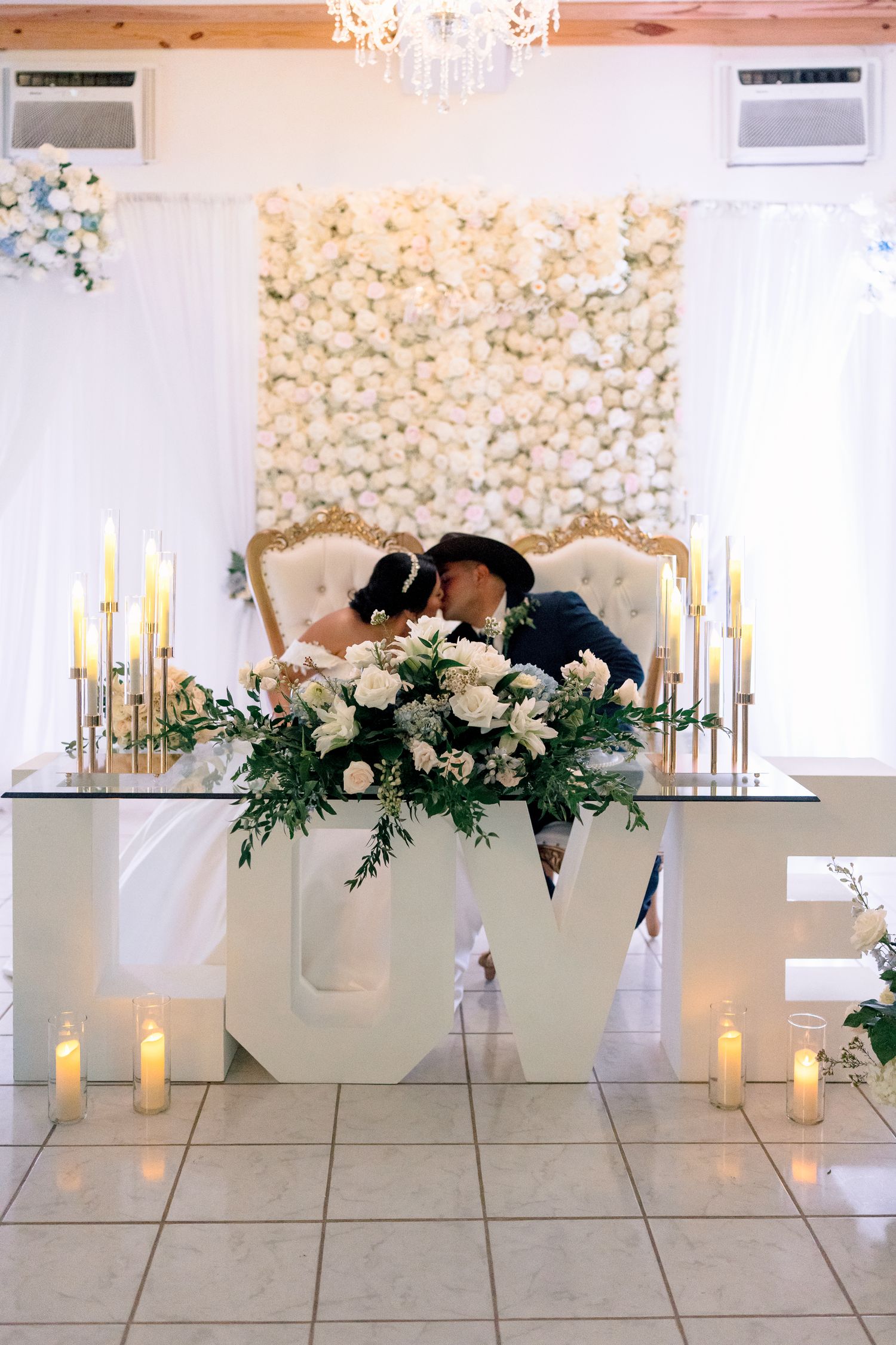Elegant wedding reception decor with white floral arrangements, candles and greenery on modern pedestals.