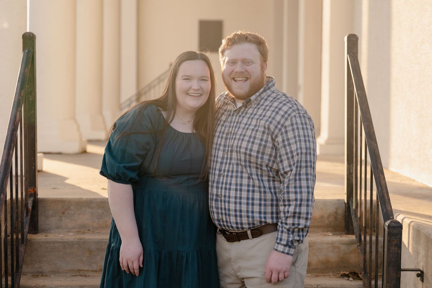 Smiling couple posing together on steps of a white columned building during engagement photos.