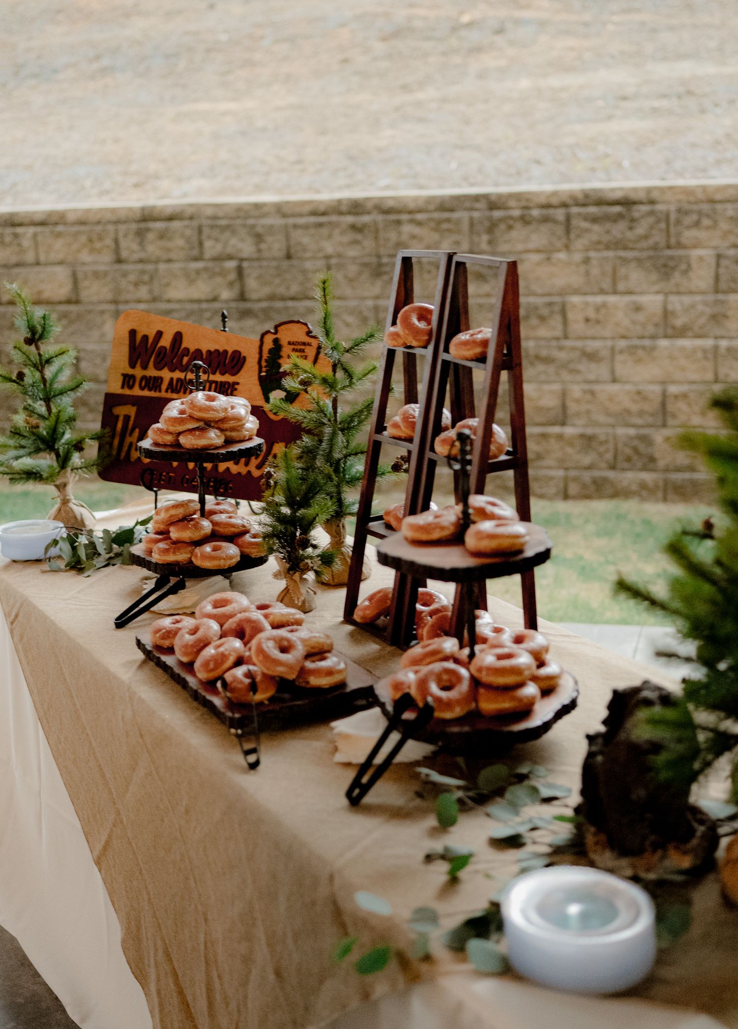 Elegant wedding donut dessert display with tiered stands and ladder rack against brick wall.