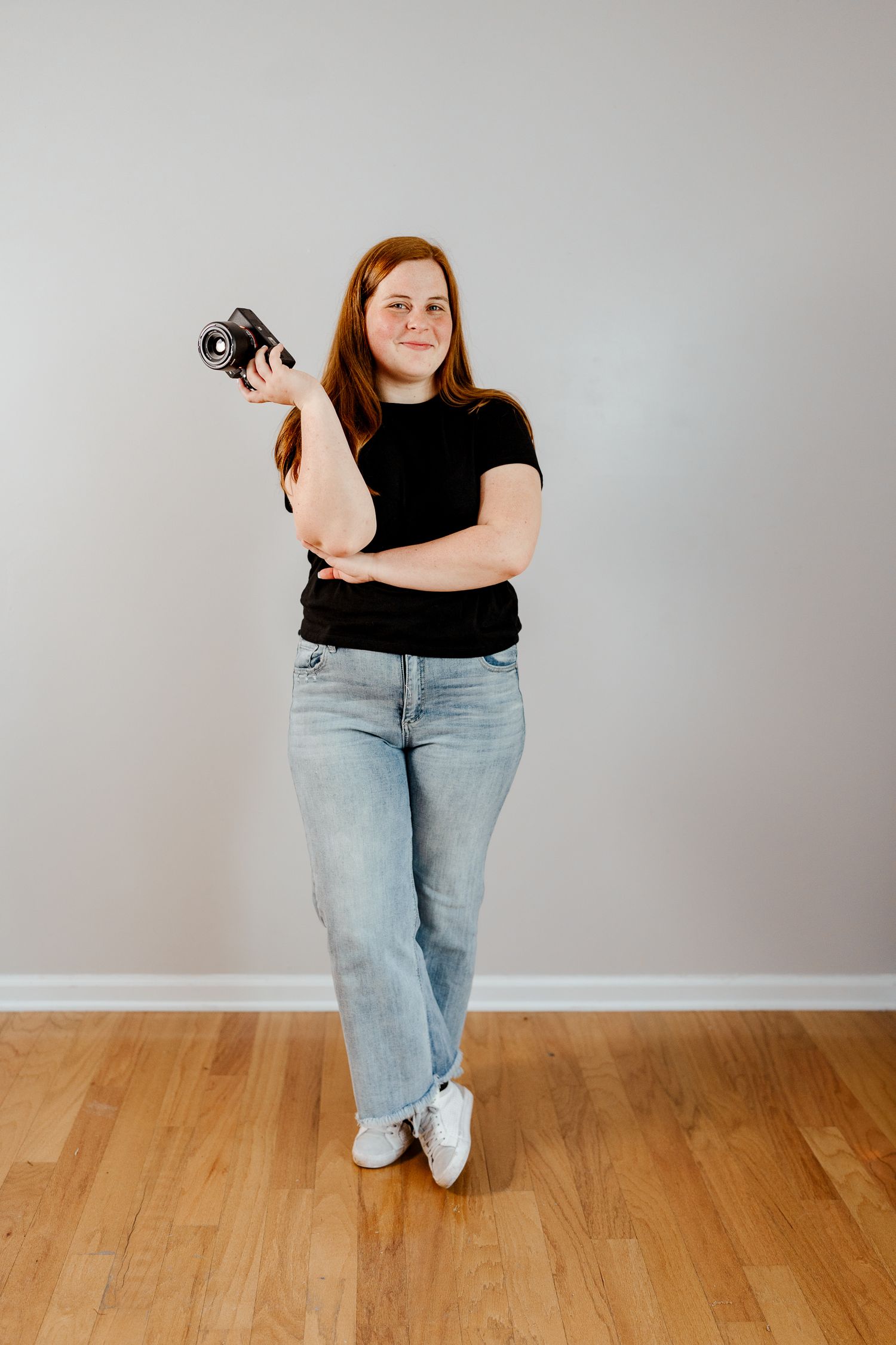 Person demonstrates various standing poses with camera against grey wall and wooden floor.