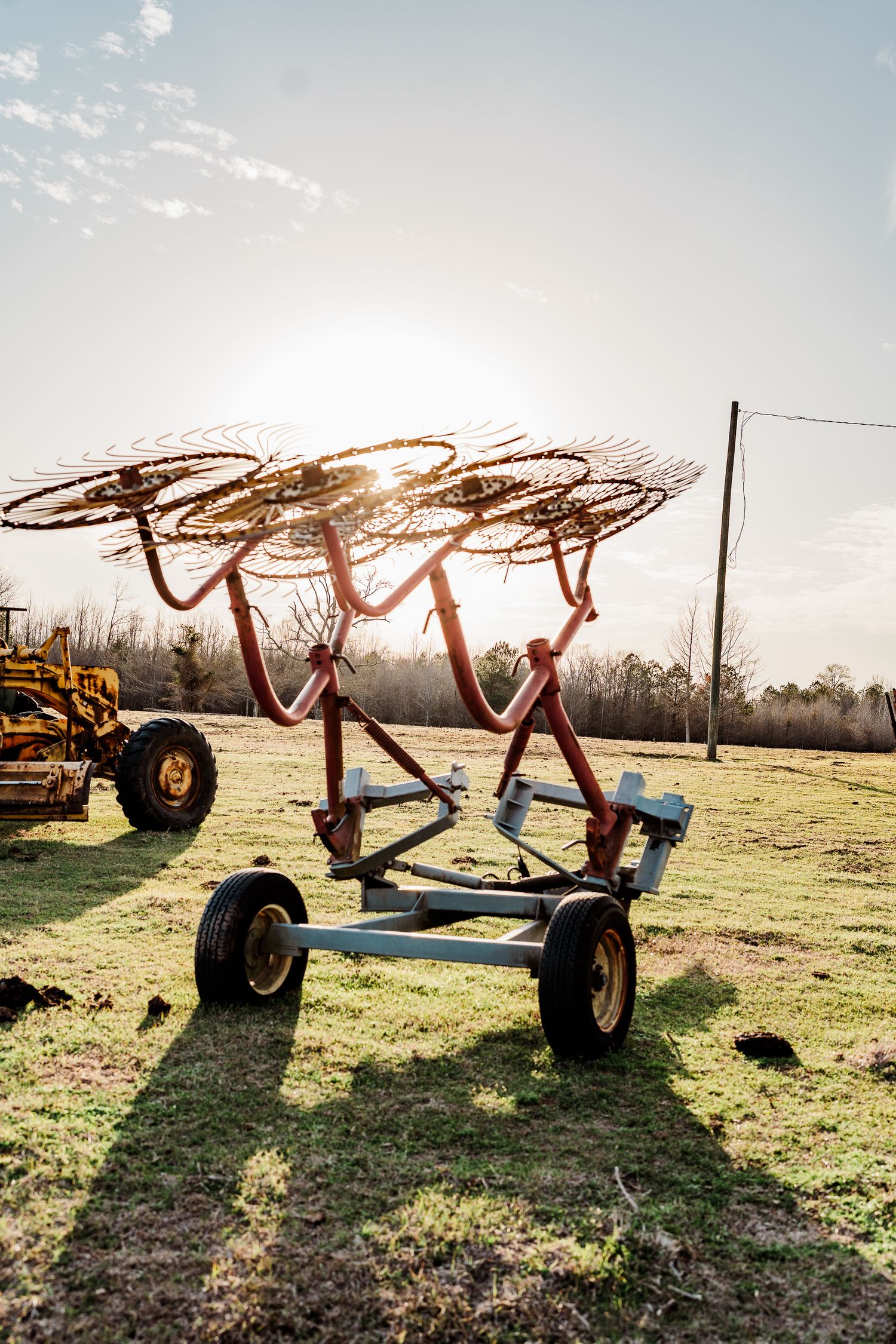 Farm equipment silhouetted against sunset with metal rake attachments visible.