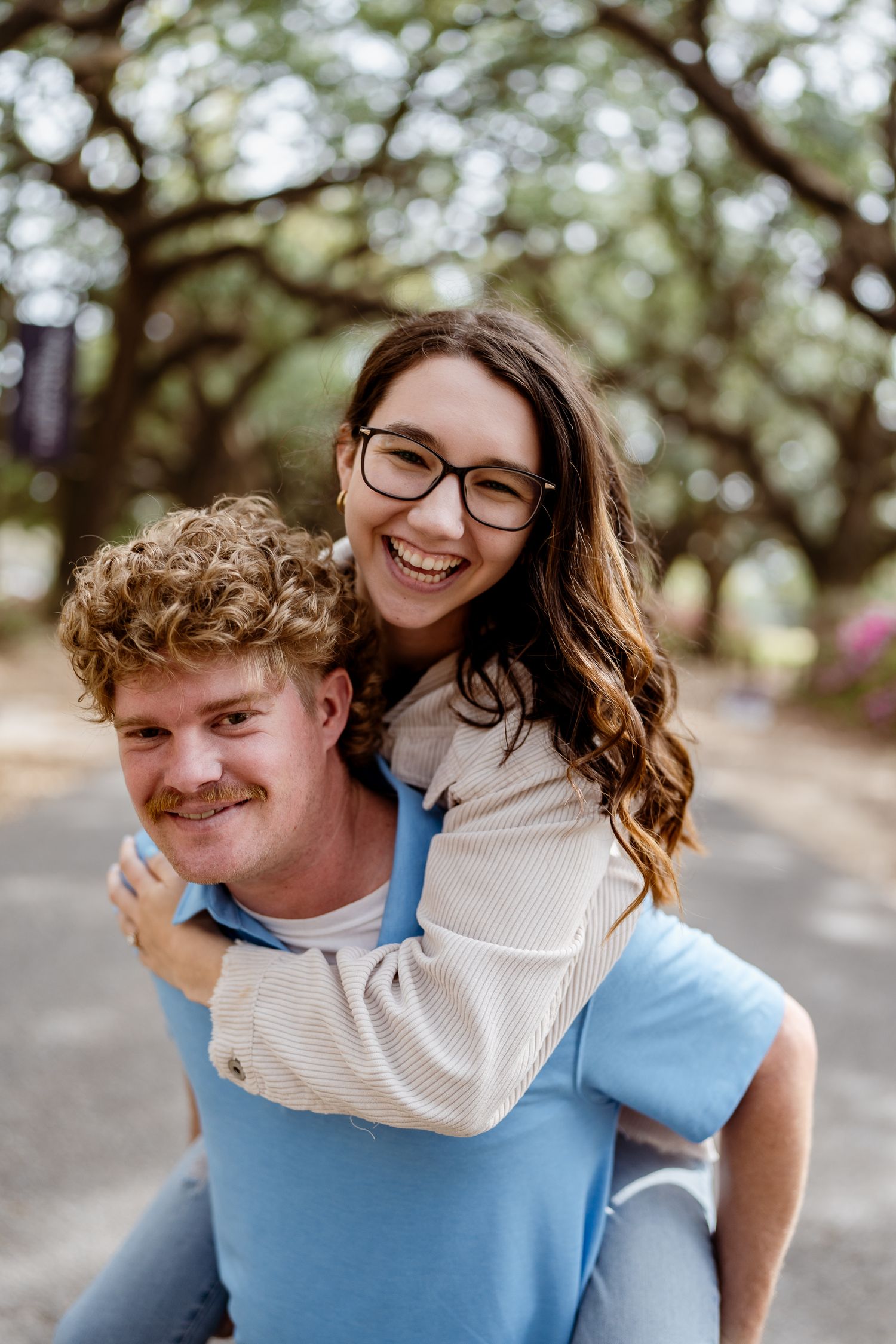 A cheerful piggyback ride moment captured under oak trees in a park setting.