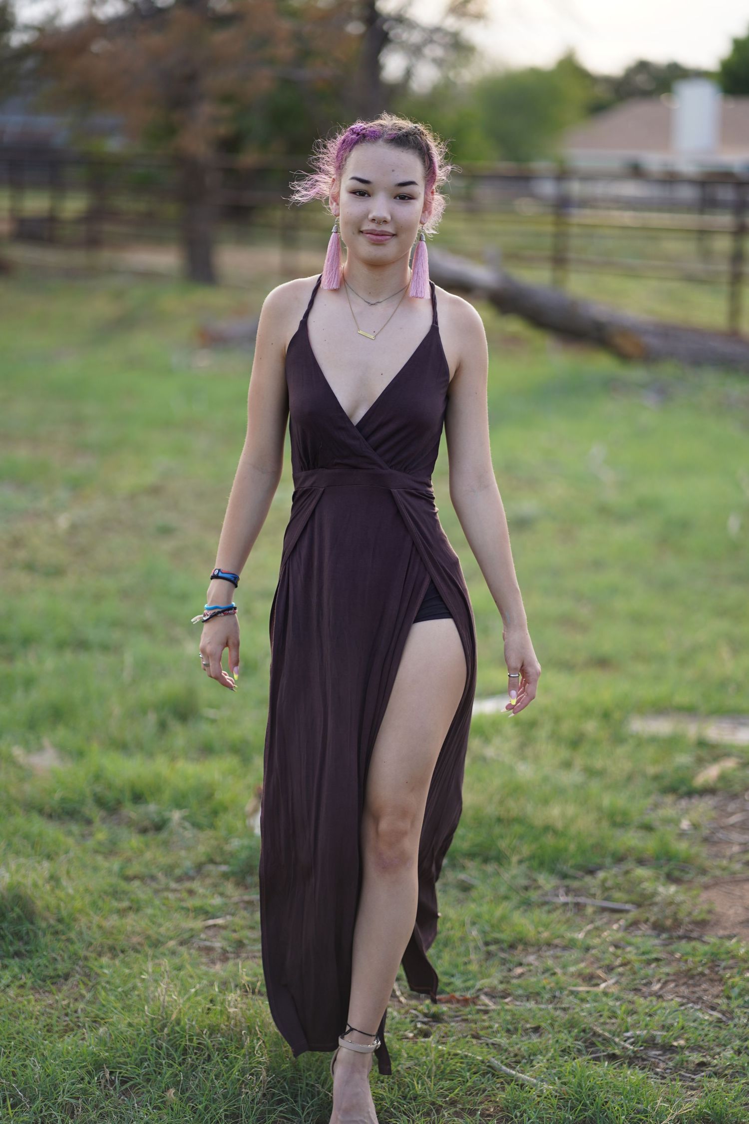 A long black maxi dress with a thigh slit is modeled outdoors against a rural backdrop with fencing.