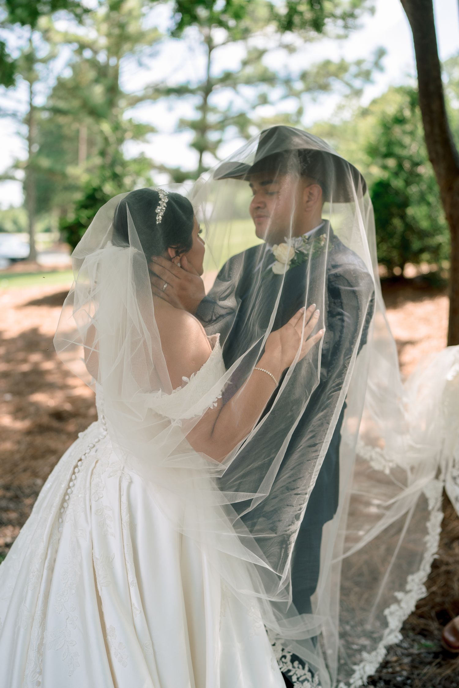 A dreamy veil shot captures an intimate wedding moment under tree canopy.