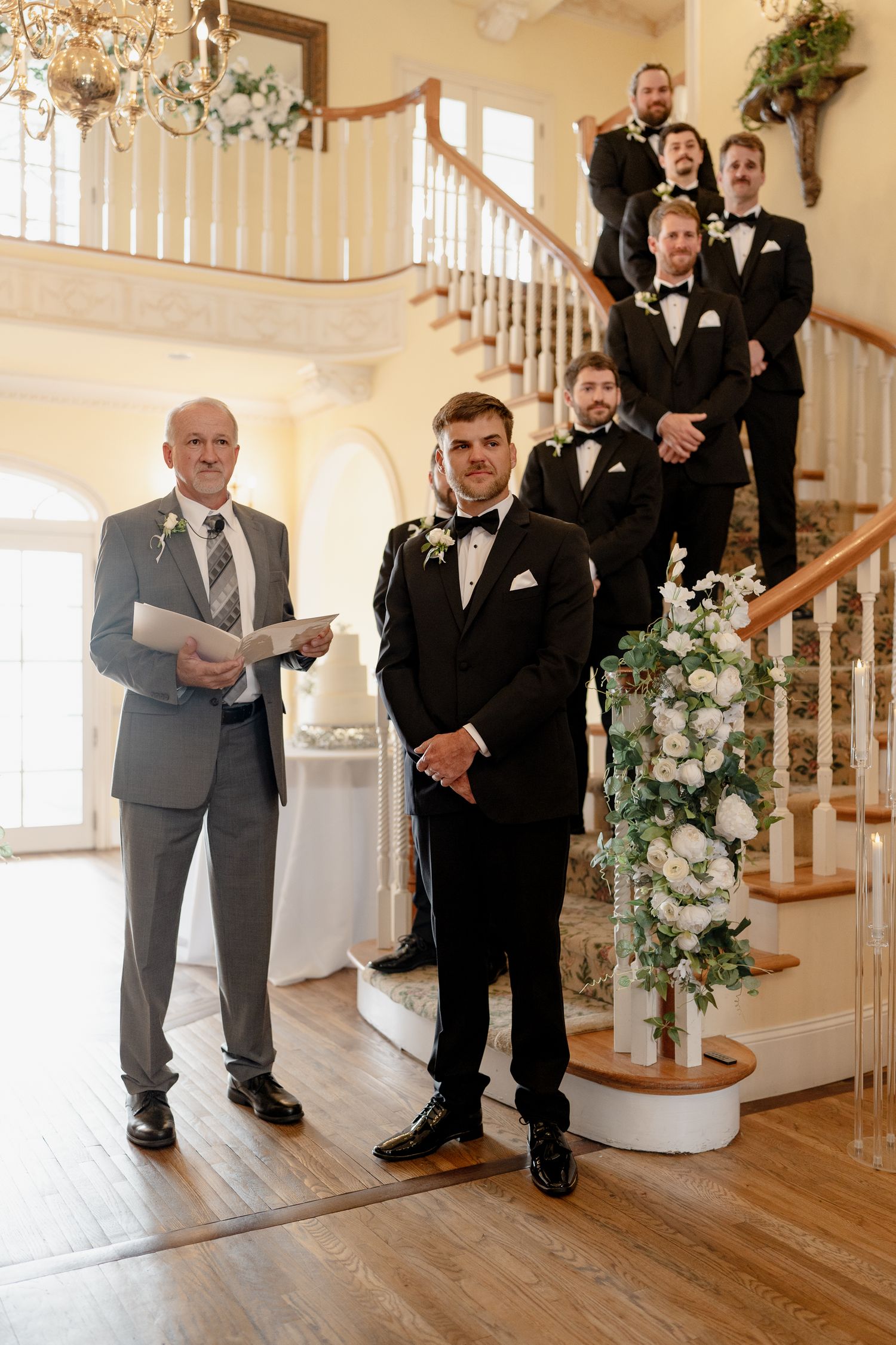 Wedding party members in formal attire pose on an elegant staircase with floral decorations.