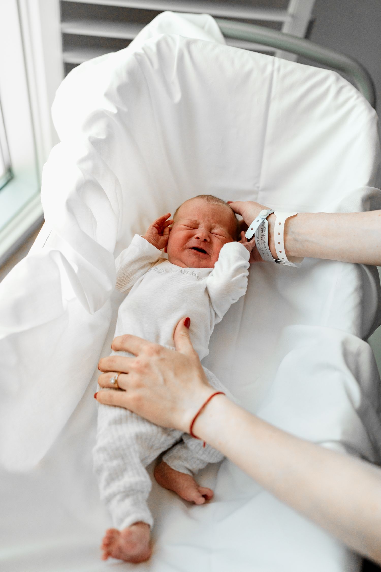 Gentle hands adjusting newborn baby's position on white bedding.