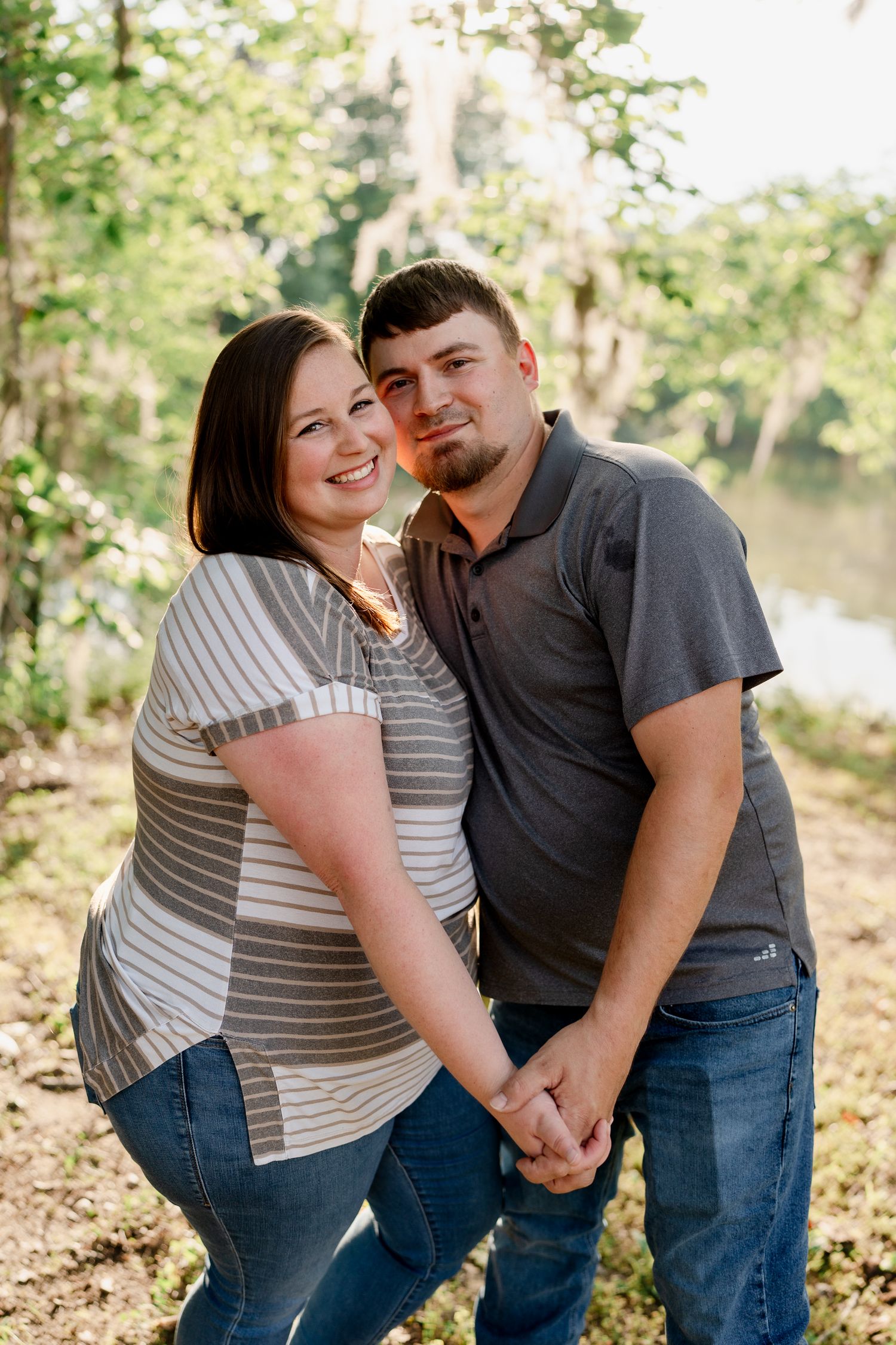 Couple embraces while laughing together in a sunlit forest setting.