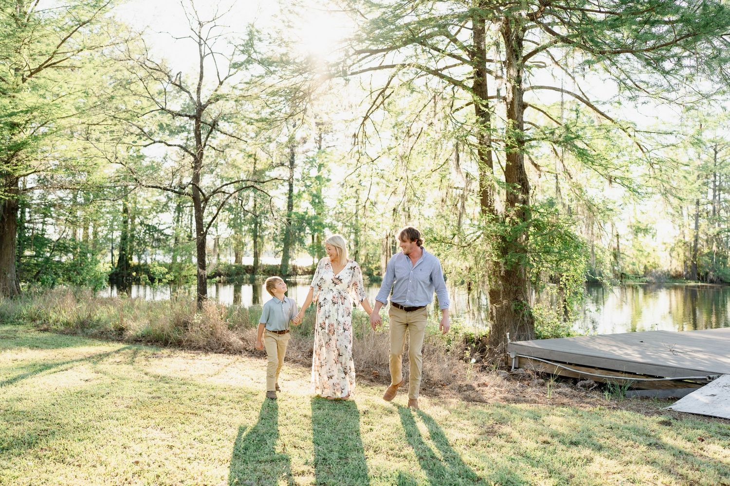 A loving family and their golden retriever pose together on a grassy lawn surrounded by sunlit trees.