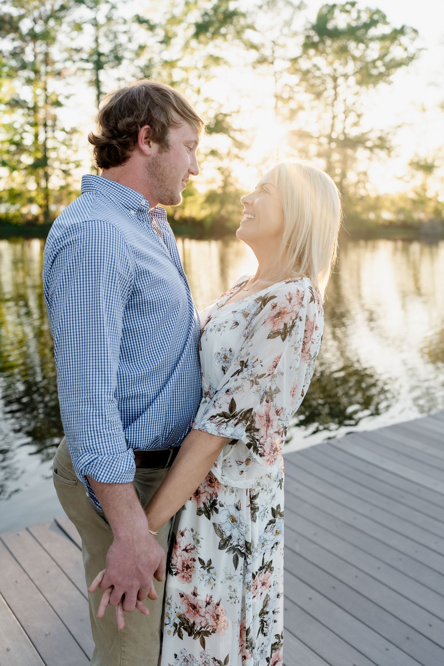 Romantic couple in casual attire sharing an intimate moment on a lakeside deck at sunset.