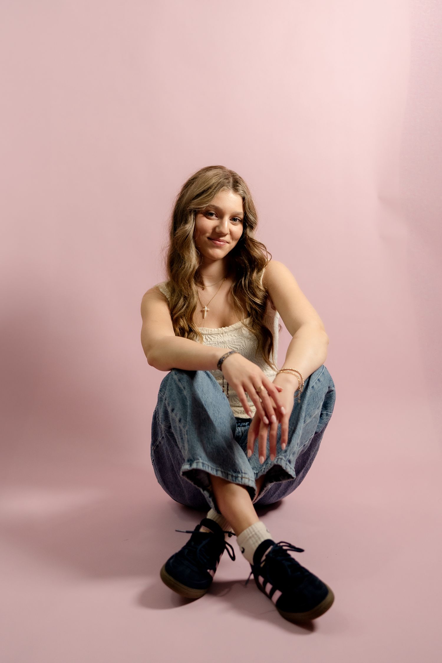 Relaxed studio portrait featuring casual denim and tank top combination on pink background.