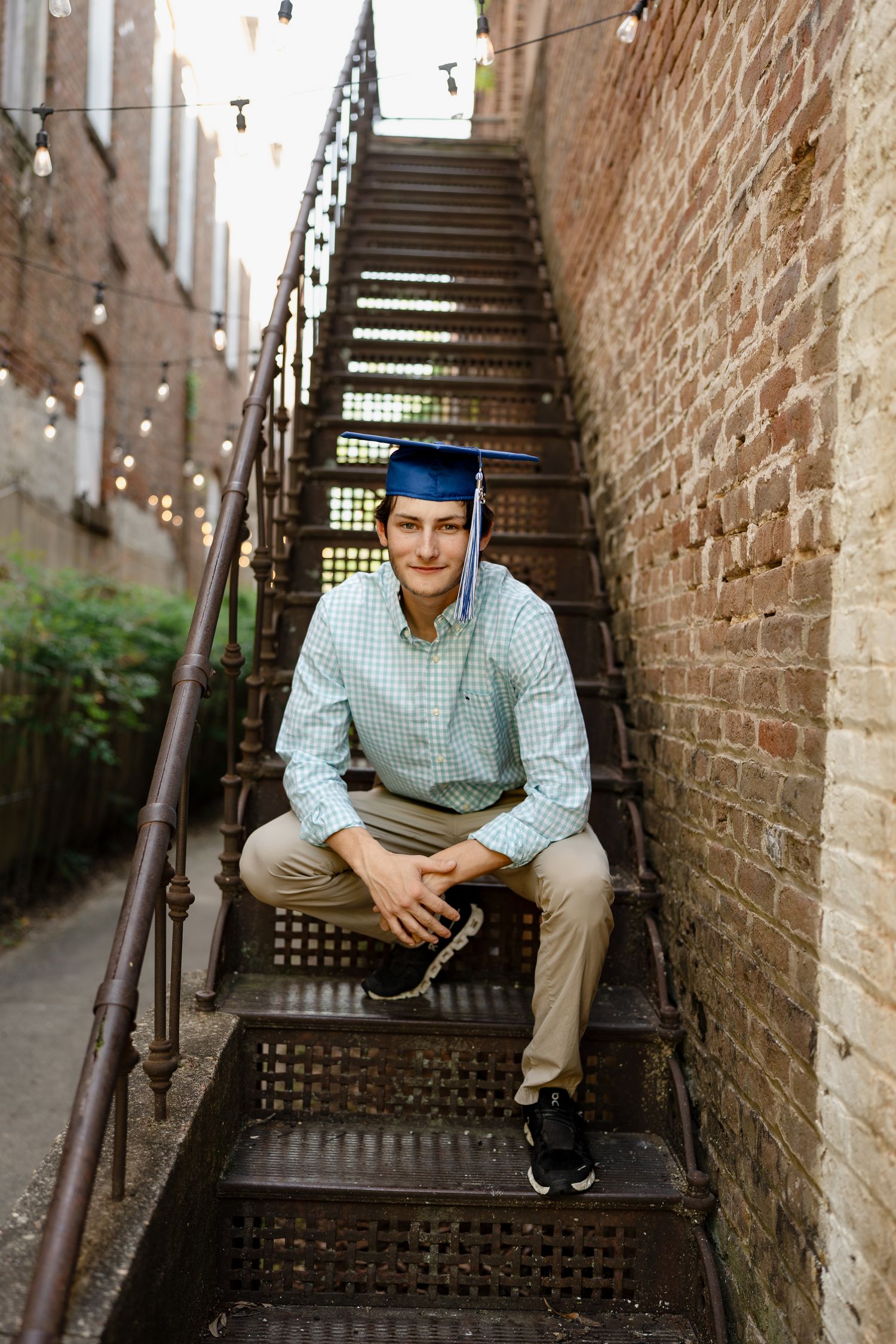 Graduate sits on industrial metal staircase during outdoor photo session.