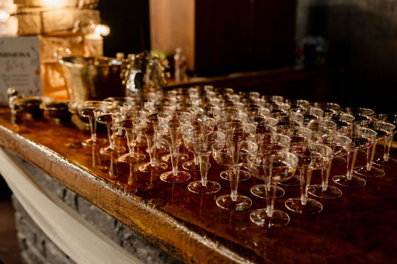 Long wooden table set with rows of empty wine glasses and eucalyptus garland for an upscale event.