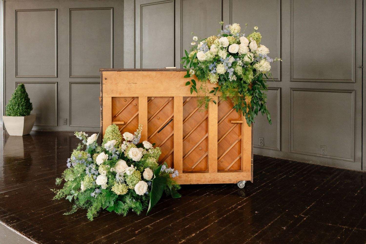 Elegant wooden crate decorated with lush white roses and greenery arrangements on dark hardwood floor.