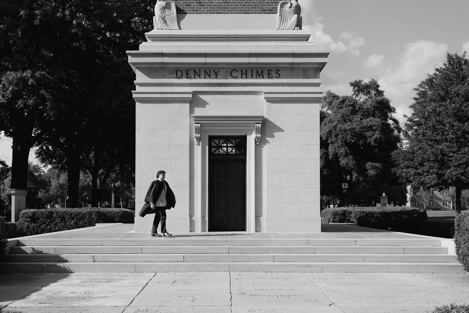 Black and white photo of a person standing at the entrance of Denny Chimes monument on a university campus.