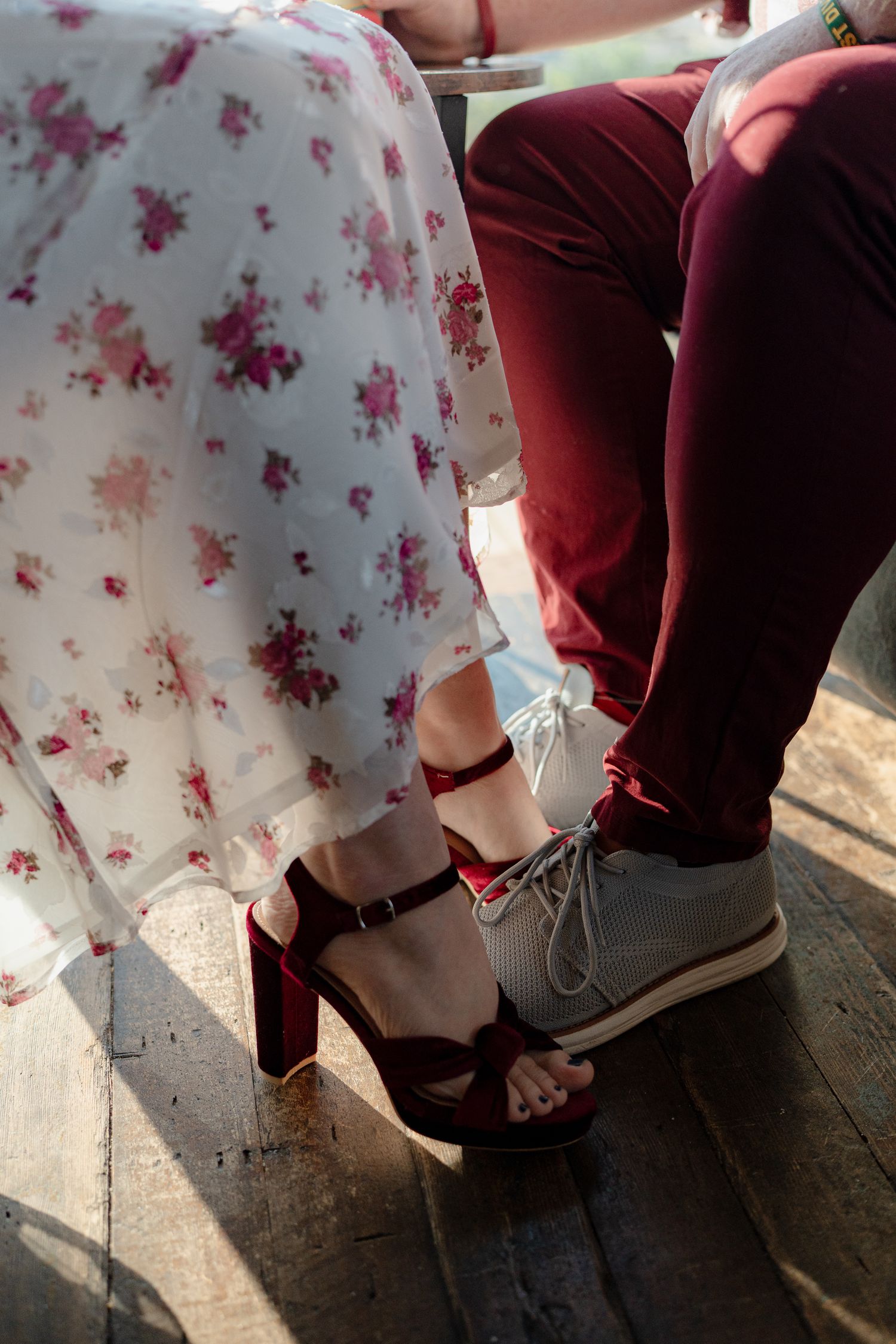 Close-up of contrasting footwear showing floral dress, burgundy pants, and red heels against gray sneakers.