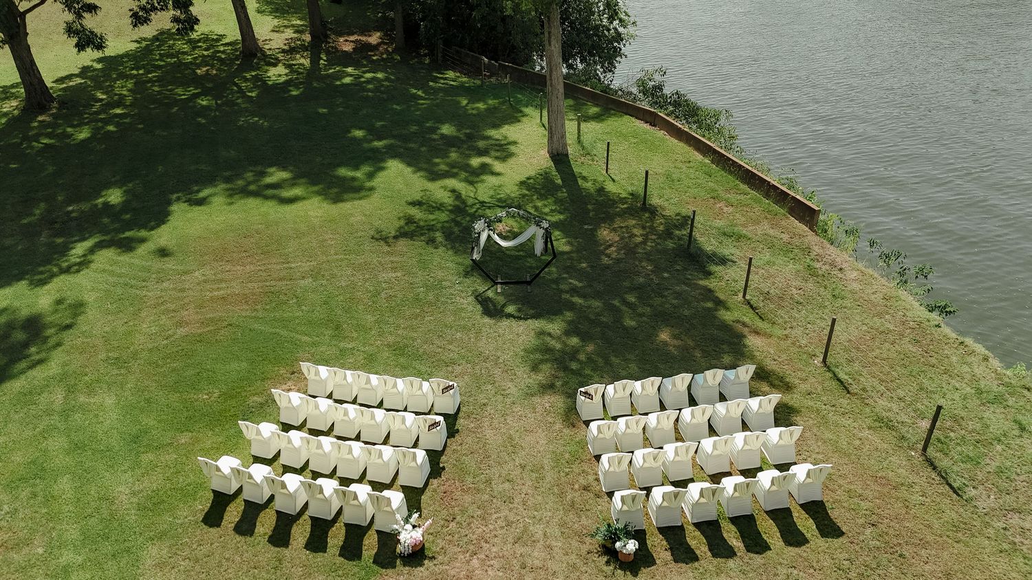 Aerial view of white chairs arranged in two sections on a waterfront lawn for an outdoor ceremony.