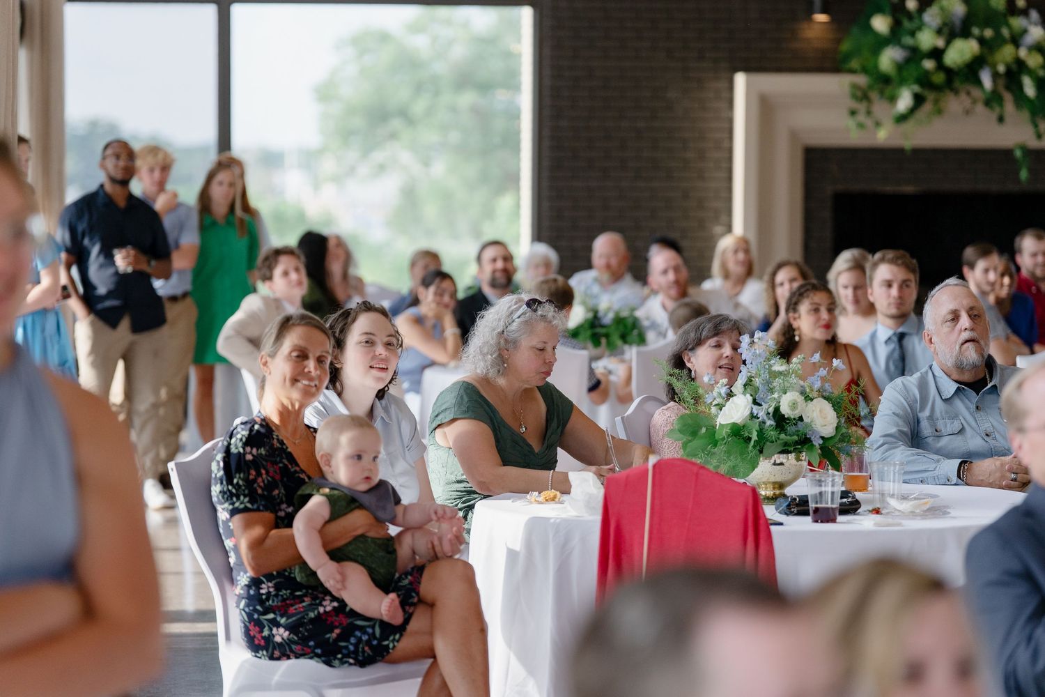 Guests celebrate at a wedding reception with round tables decorated with white floral centerpieces in an elegant venue.