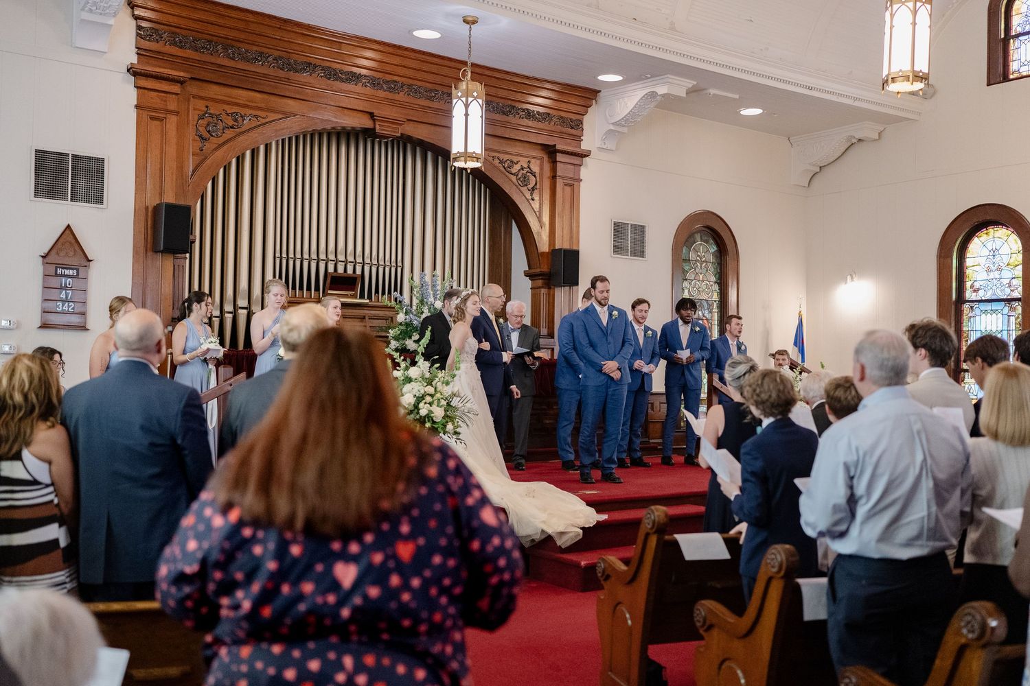 Wedding ceremony taking place at the altar of a church with wooden organ pipes and arched architecture.
