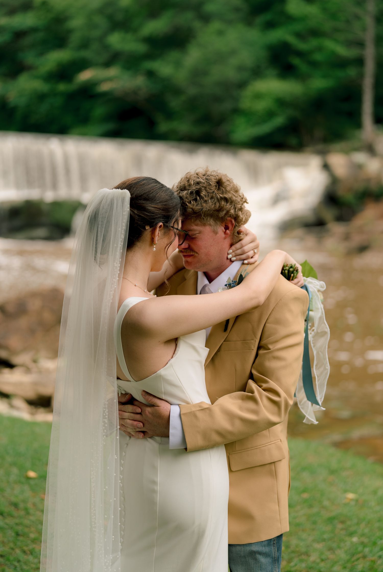 Bride and groom share romantic kiss in front of scenic waterfall on their wedding day.