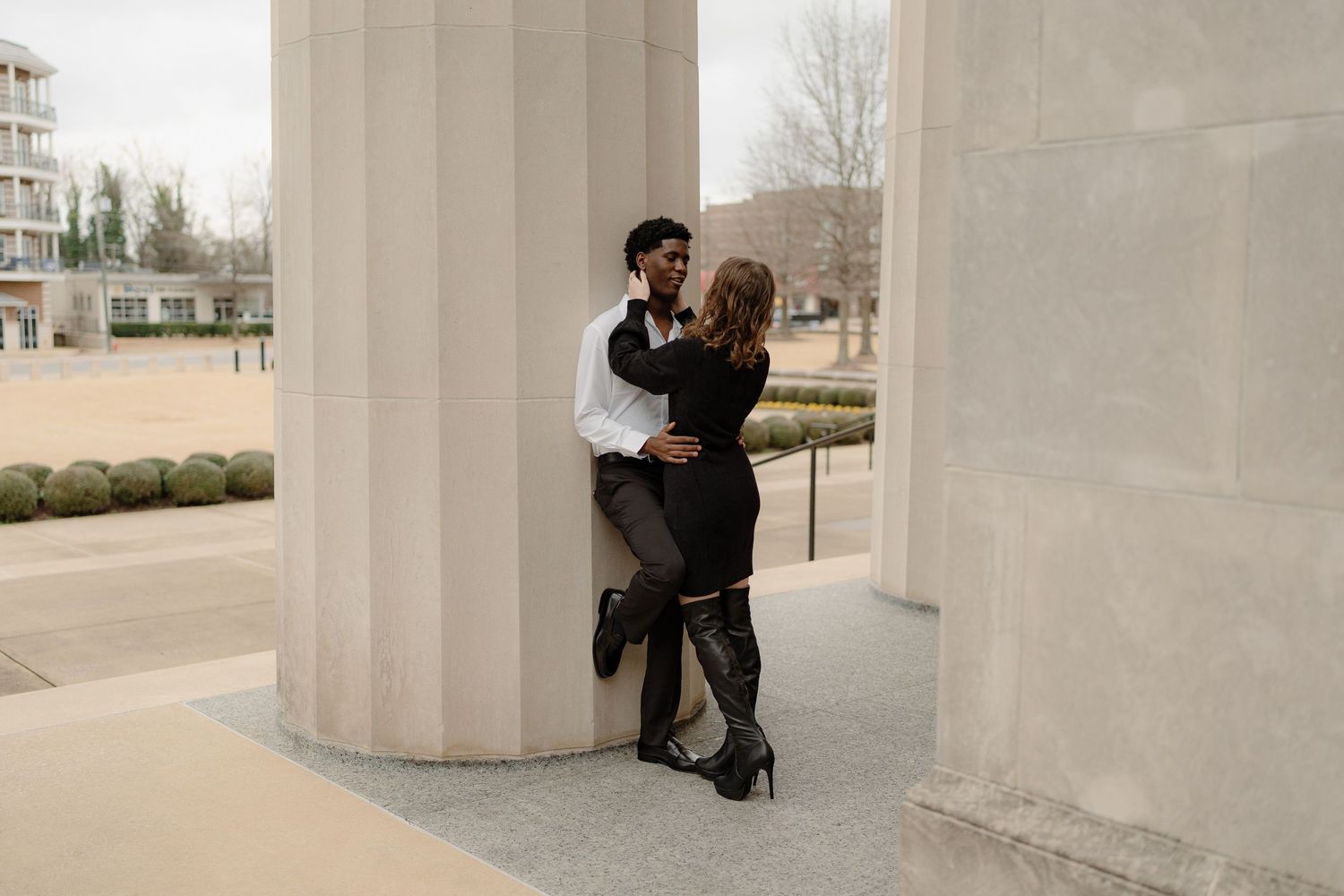 Couple sharing a romantic moment leaning against a large white column at an outdoor monument.