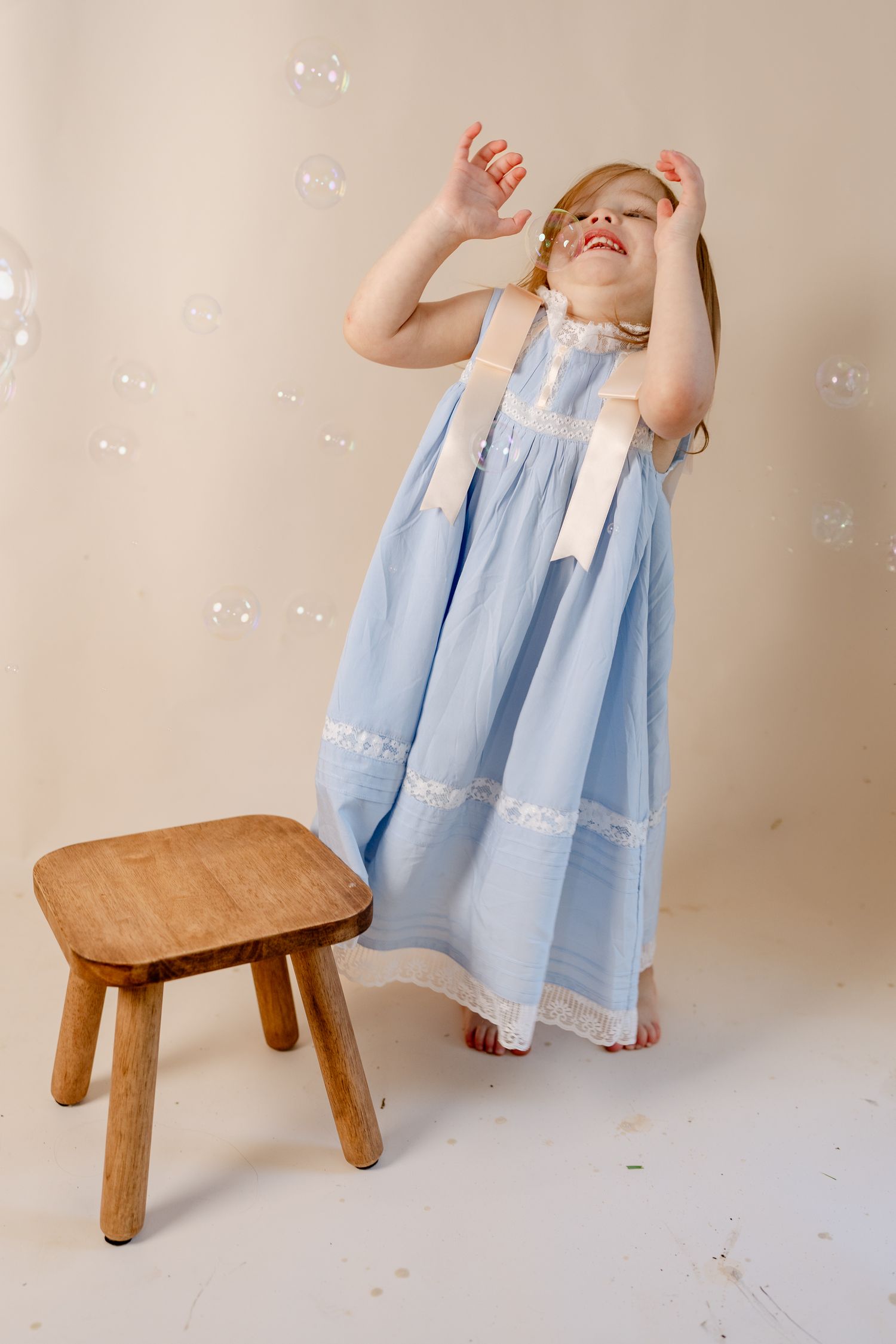 Soap bubbles float around a wooden stool against a cream colored studio backdrop.