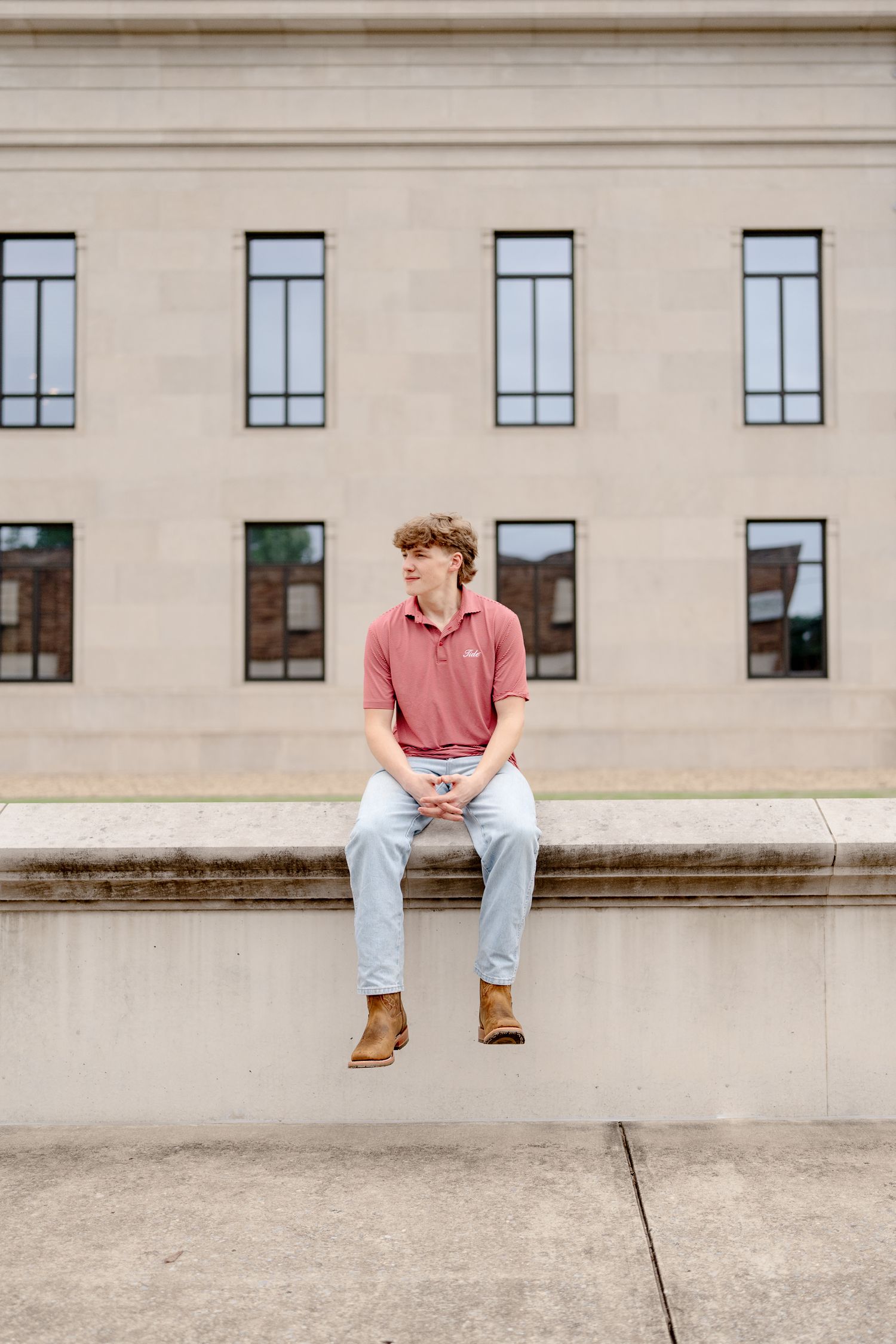 Person seated on concrete ledge against backdrop of institutional building with uniform windows.