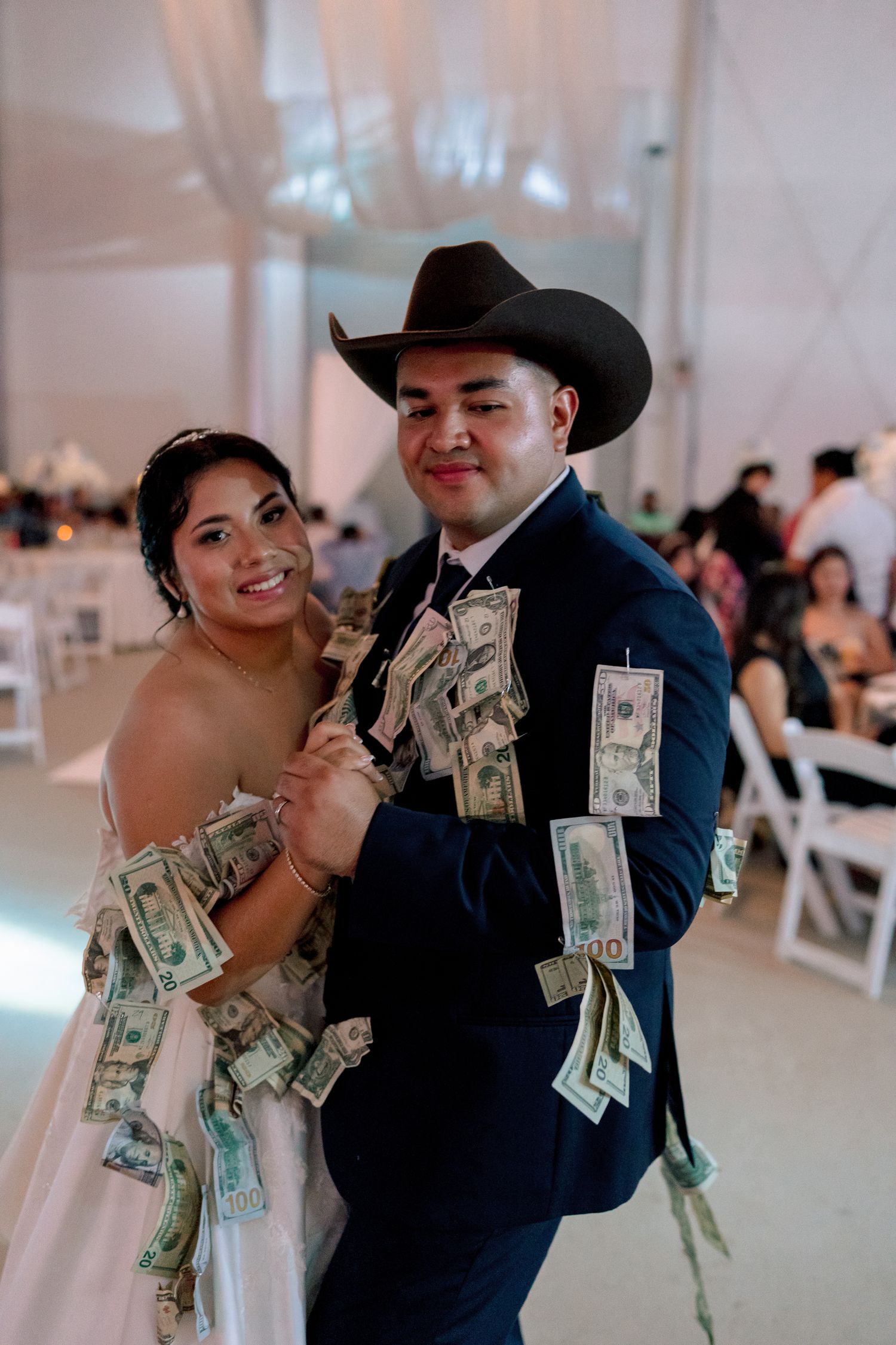 Wedding celebration showing guests dancing with money in a festive reception hall.