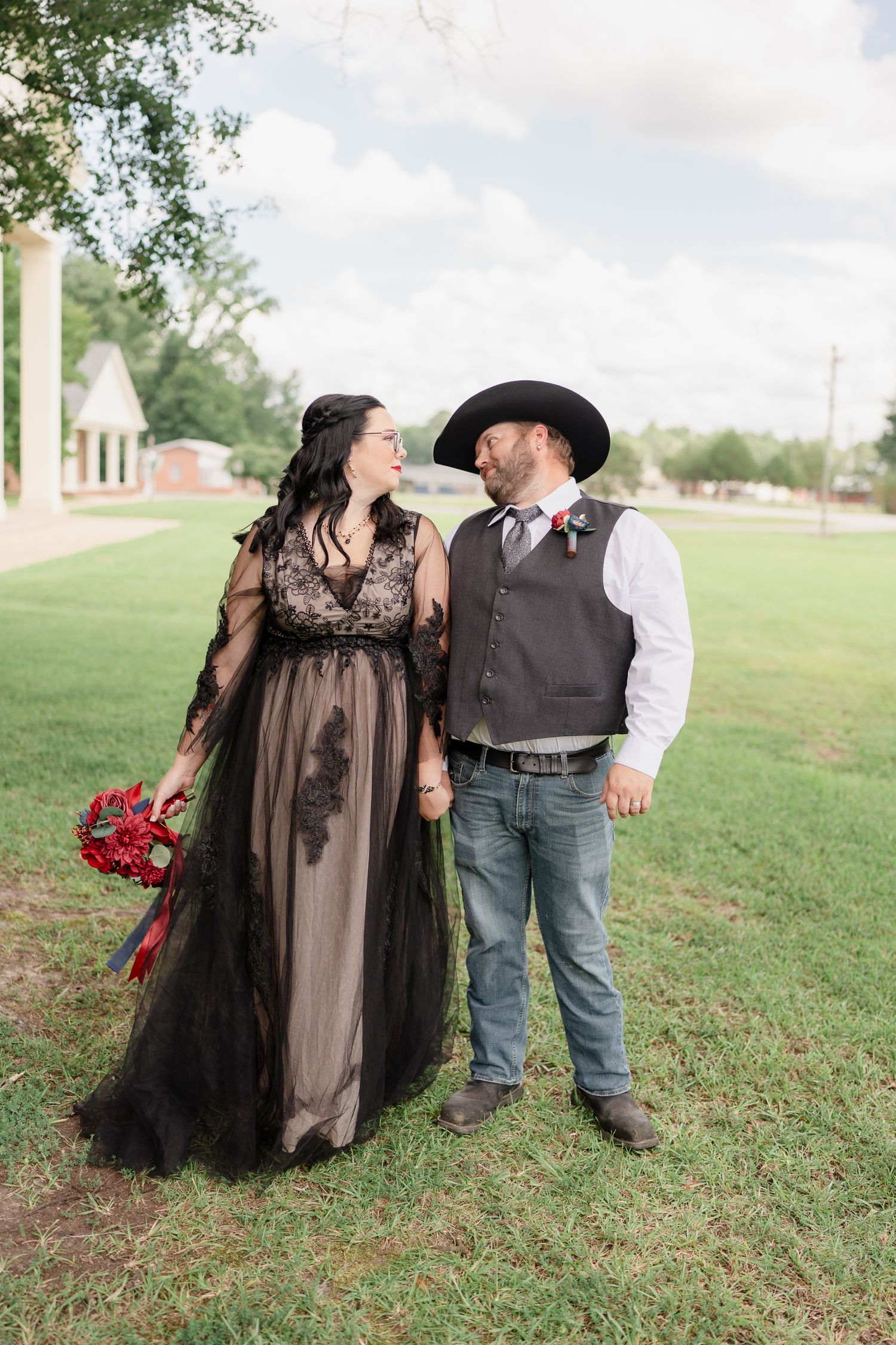 Couple in black dress and western wear poses together on grassy hillside.