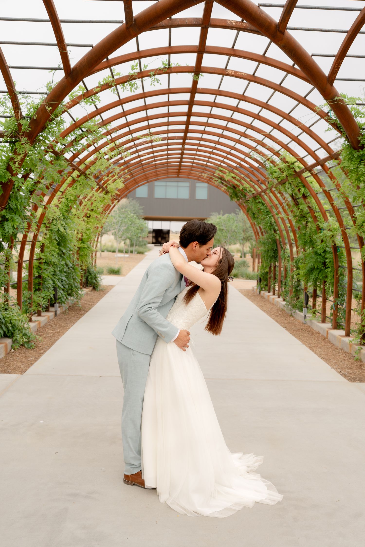 A romantic wedding moment captured in a beautiful arched greenhouse walkway with natural lighting.