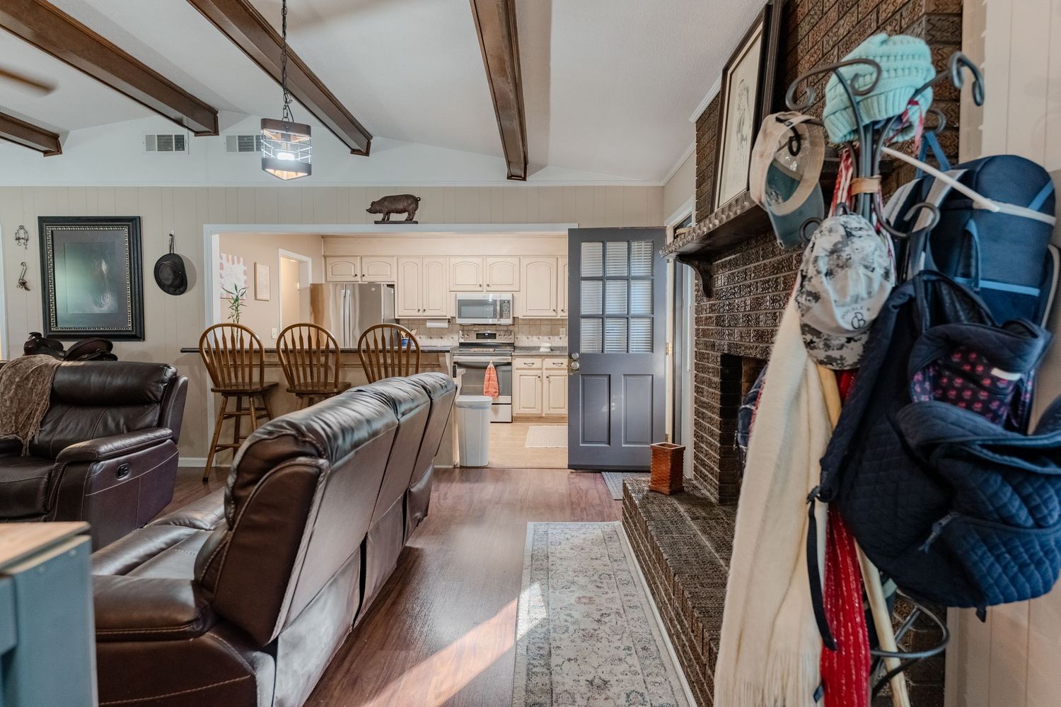 Open concept living space with leather furniture, wooden beams, and view into dining area and kitchen.