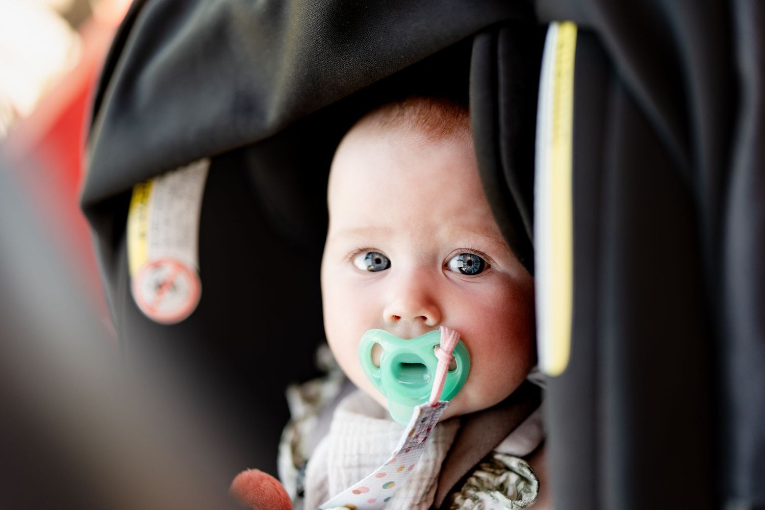 A baby with a pacifier looks up with wide-eyed curiosity while wearing a white outfit.