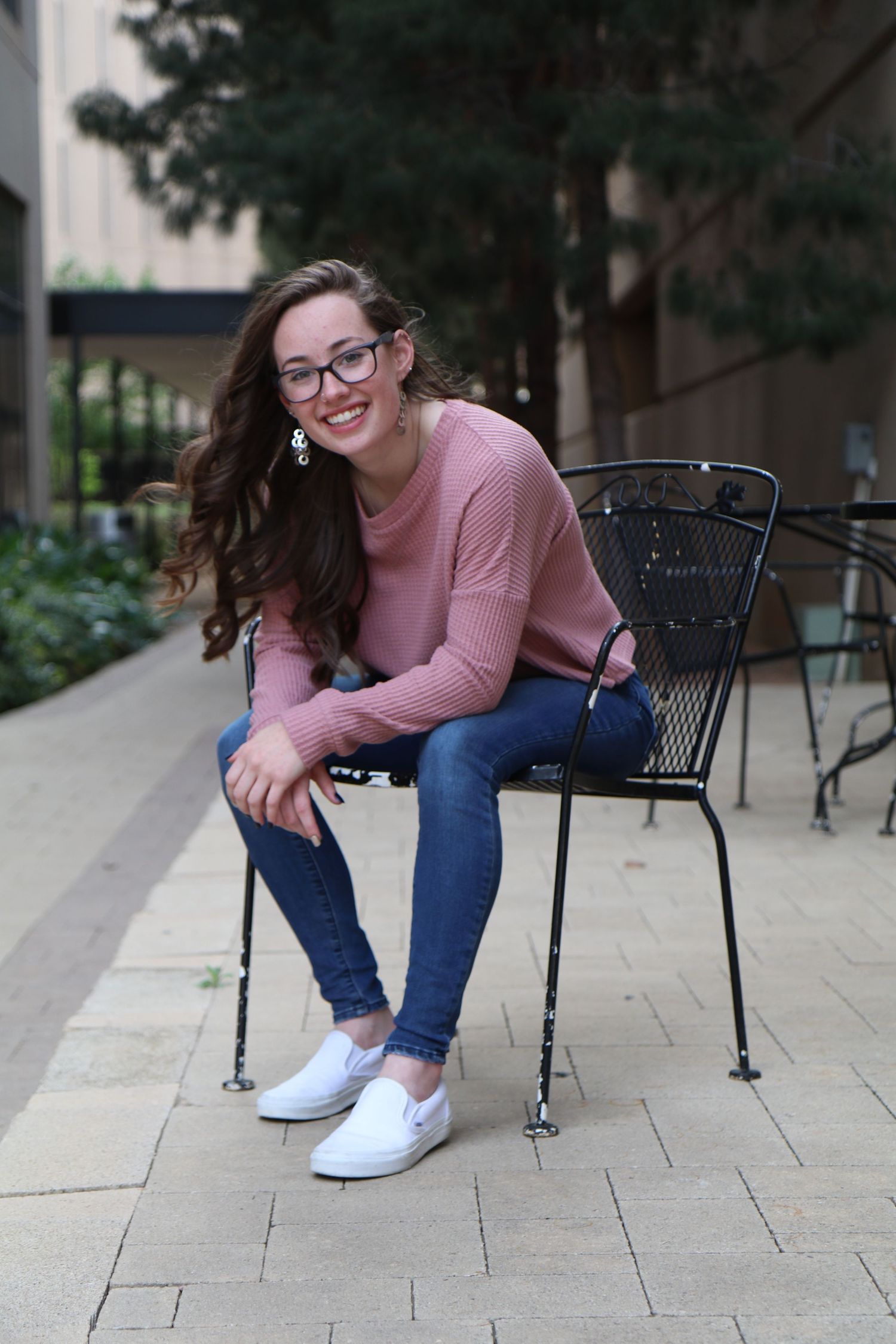 Casual outdoor portrait on metal chair wearing pink sweater and jeans.